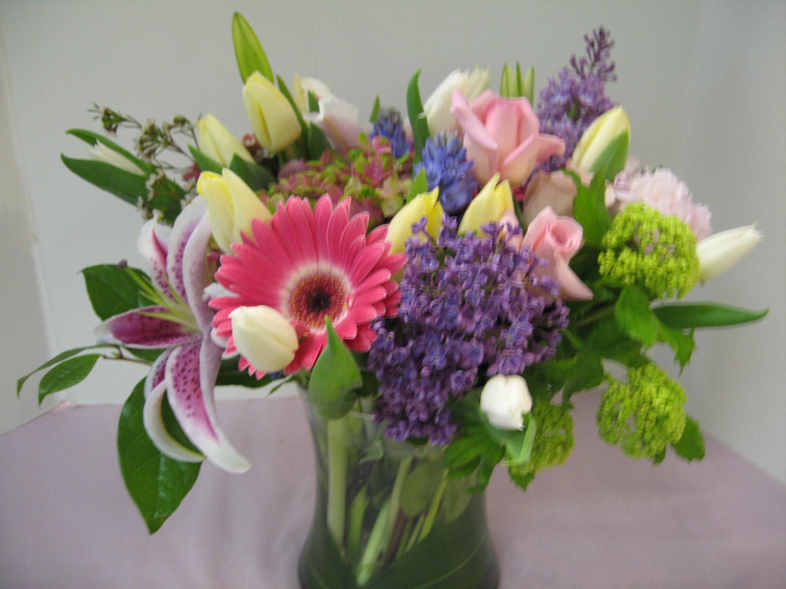 Mixed bouquet of pink gerbera, lilies, roses, tulips, and purple flowers in a clear glass vase
