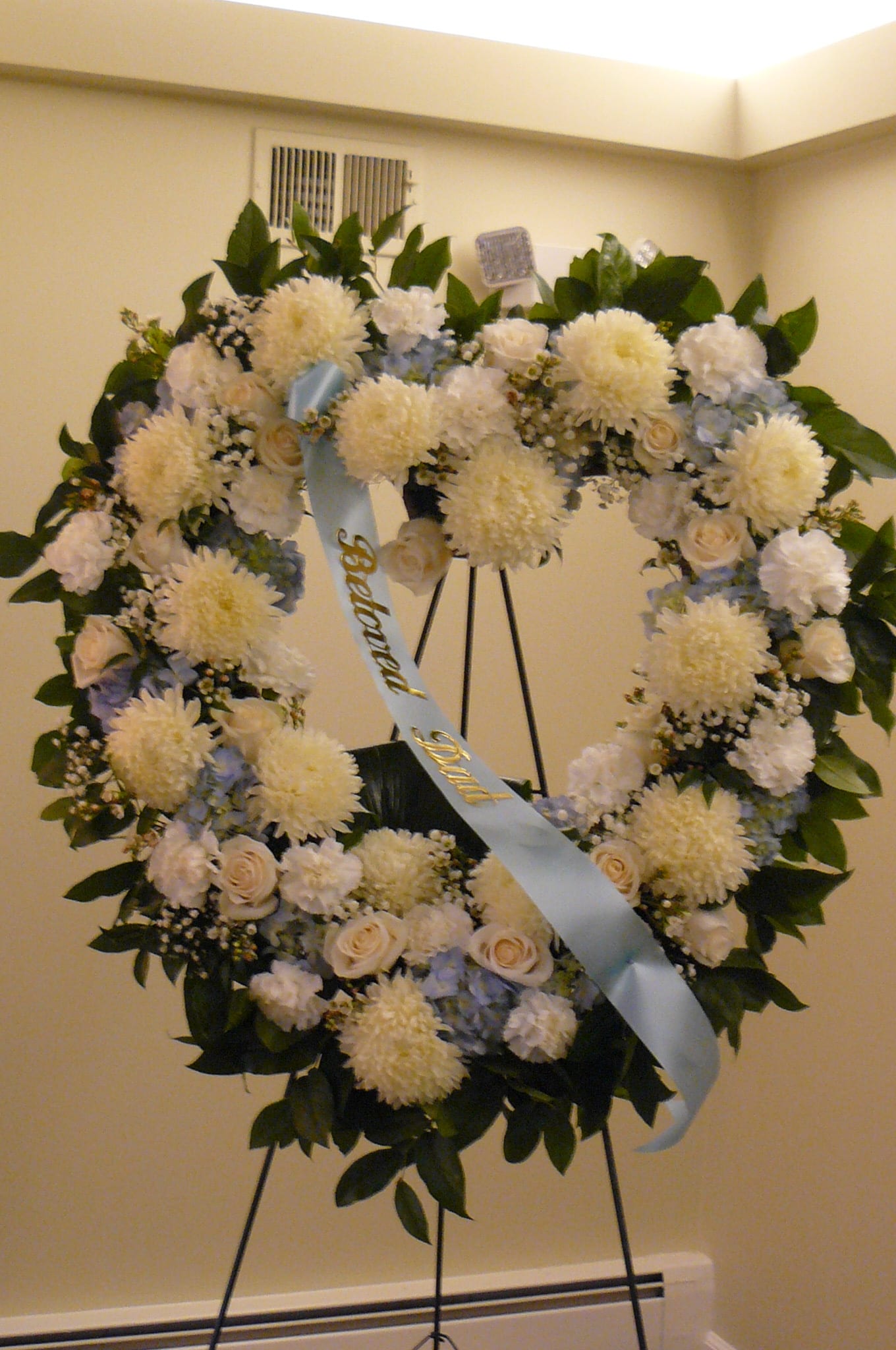 Heart-shaped funeral wreath with white flowers and a blue ribbon on an easel