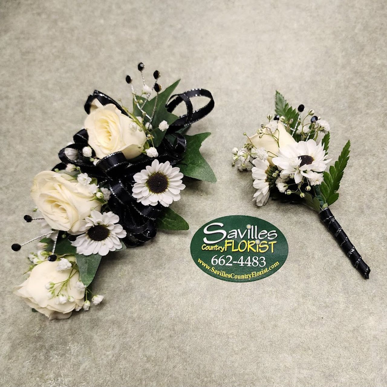 Two white floral boutonnieres with black ribbon accents on a gray surface