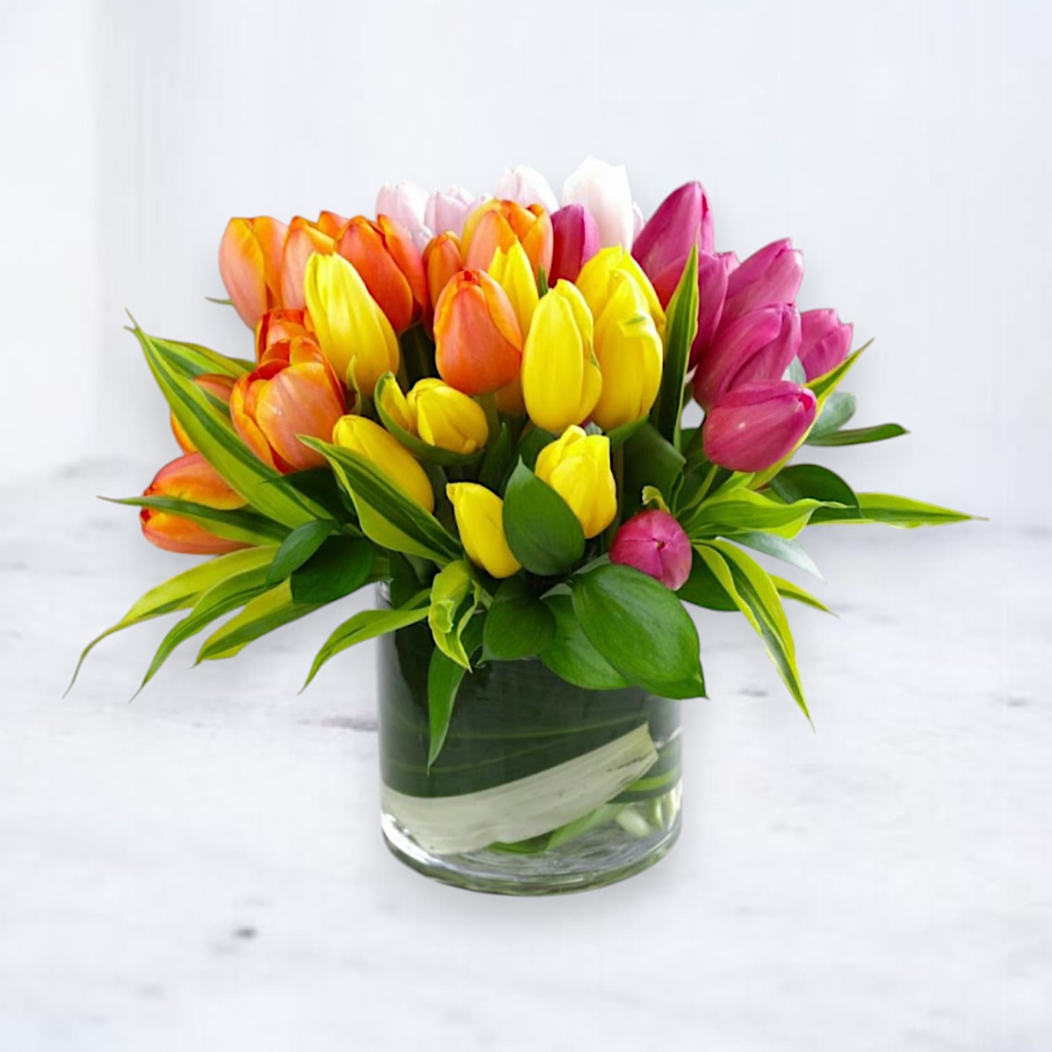 Tulip Jubilee - Brighten any day with the Tulip Jubilee, a radiant celebration of color and joy. This stunning floral arrangement showcases a vibrant mix of fresh tulips in cheerful shades of yellow, orange, pink, and white, elegantly arranged in a sleek glass vase with lush greenery for a polished and modern look.  Perfect for birthdays, celebrations, or simply bringing a burst of happiness into someone's life, the Tulip Jubilee is a delightful statement of freshness and elegance. Available for same-day delivery in Houston and surrounding areas, this tulip arrangement is the ultimate way to spread cheer and warmth.