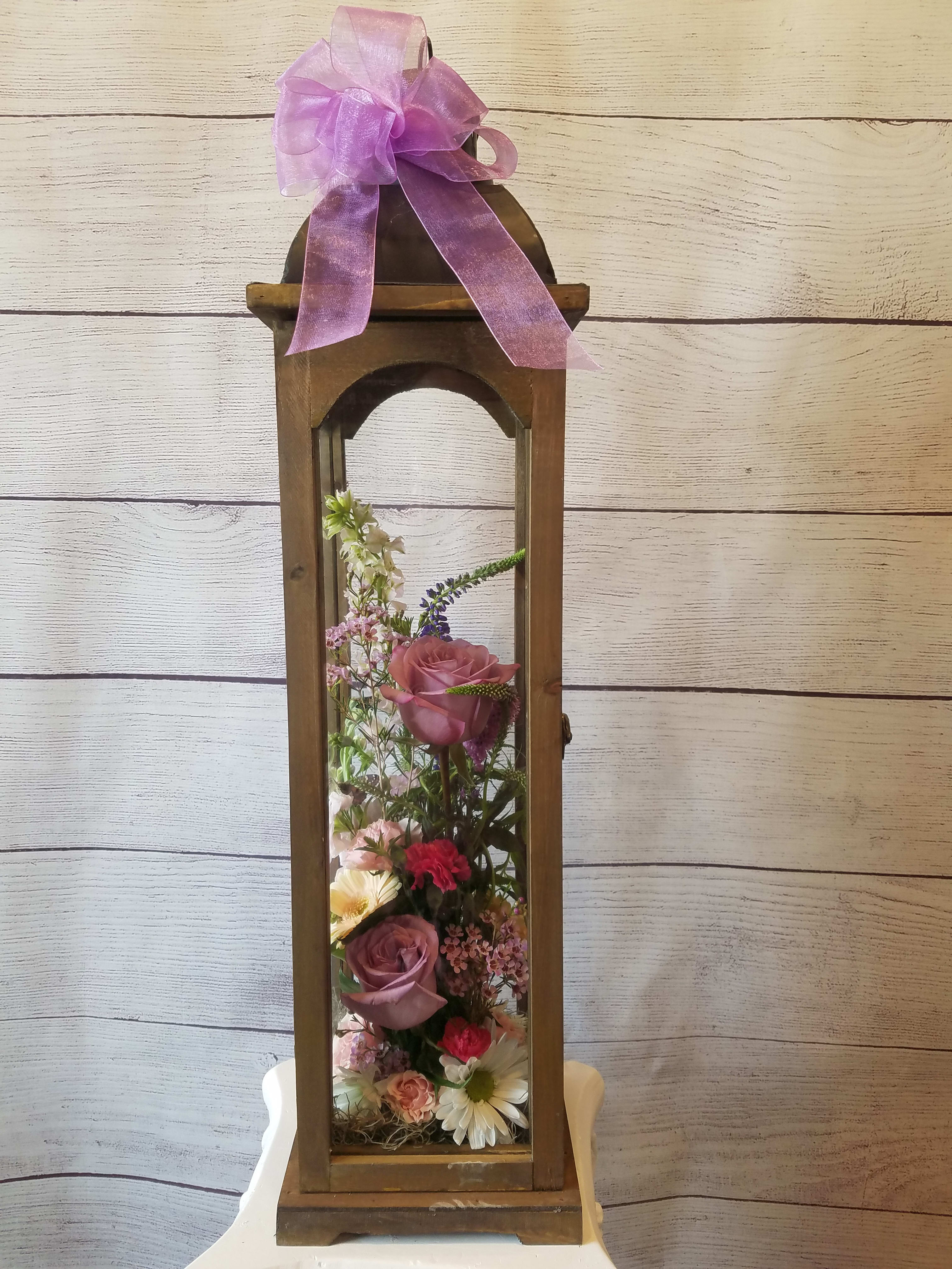 Tall wooden lantern with a pink ribbon and mixed flowers inside
