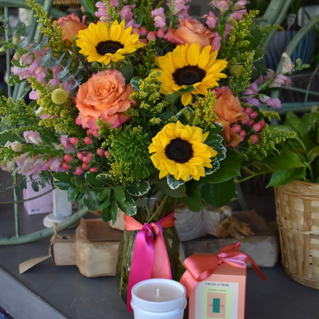 She Deserves To Be Celebrated Gift Bundle - Show your appreciation with our bright and tall composition of sunflowers, free spirit roses, pink snapdragons, craspedia, hypericum, dianthus, and solidago in a 9” Jordan vase, paired with the Mersea Fresh Citron Candle - A vibrant burst of citrus paired with subtle herbal notes creates an energizing blend that captures the essence of a sunlit garden. The delicate ylang ylang blossom introduces a floral sweetness, adding depth and sophistication. Clean and bright, this scent is pure sunshine.