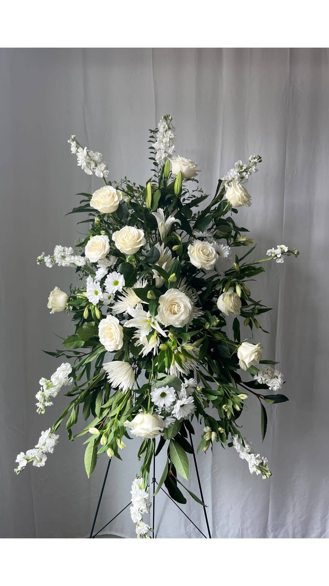 Tall white floral standing spray with roses and daisies on a black easel