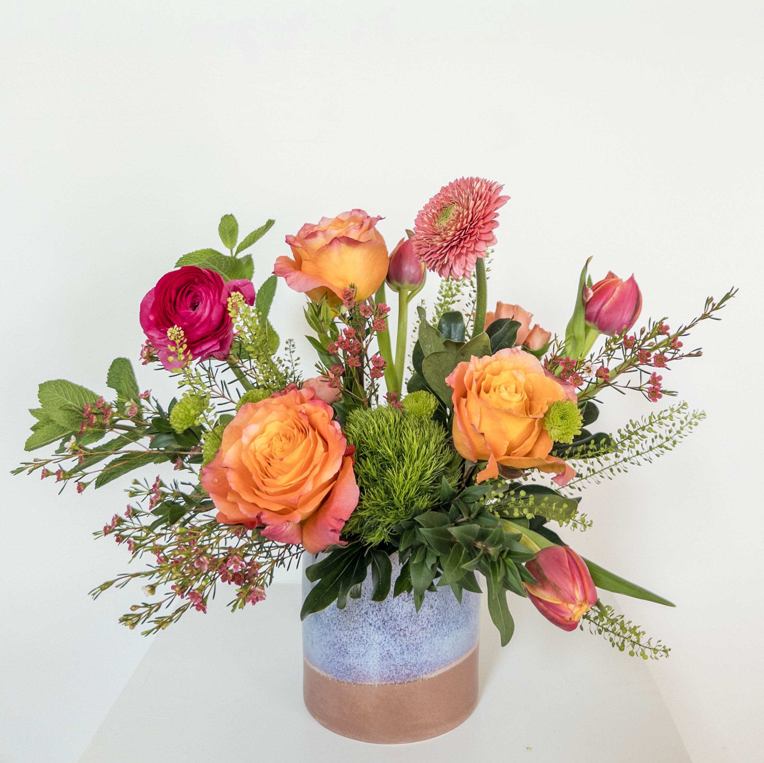 Hummingbird Charm - These vibrantly hued blooms are a total show stopper in a complimentary ceramic vessel. Arrangement includes roses, tulips, and ranunculus.   Upgrade to deluxe and premium for a larger design with more premium blooms.
