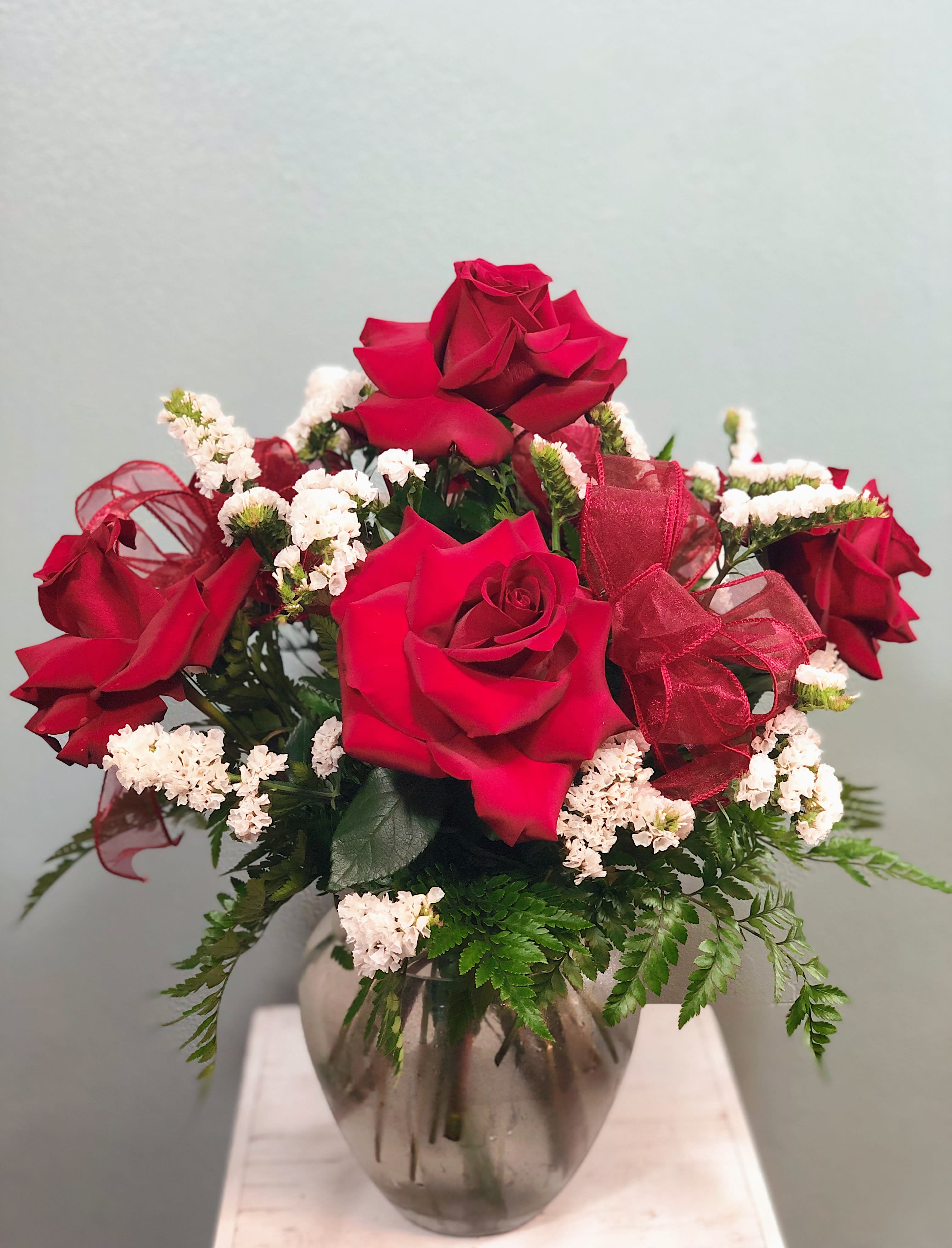 Red roses arranged in a glass vase with white filler flowers and a red ribbon