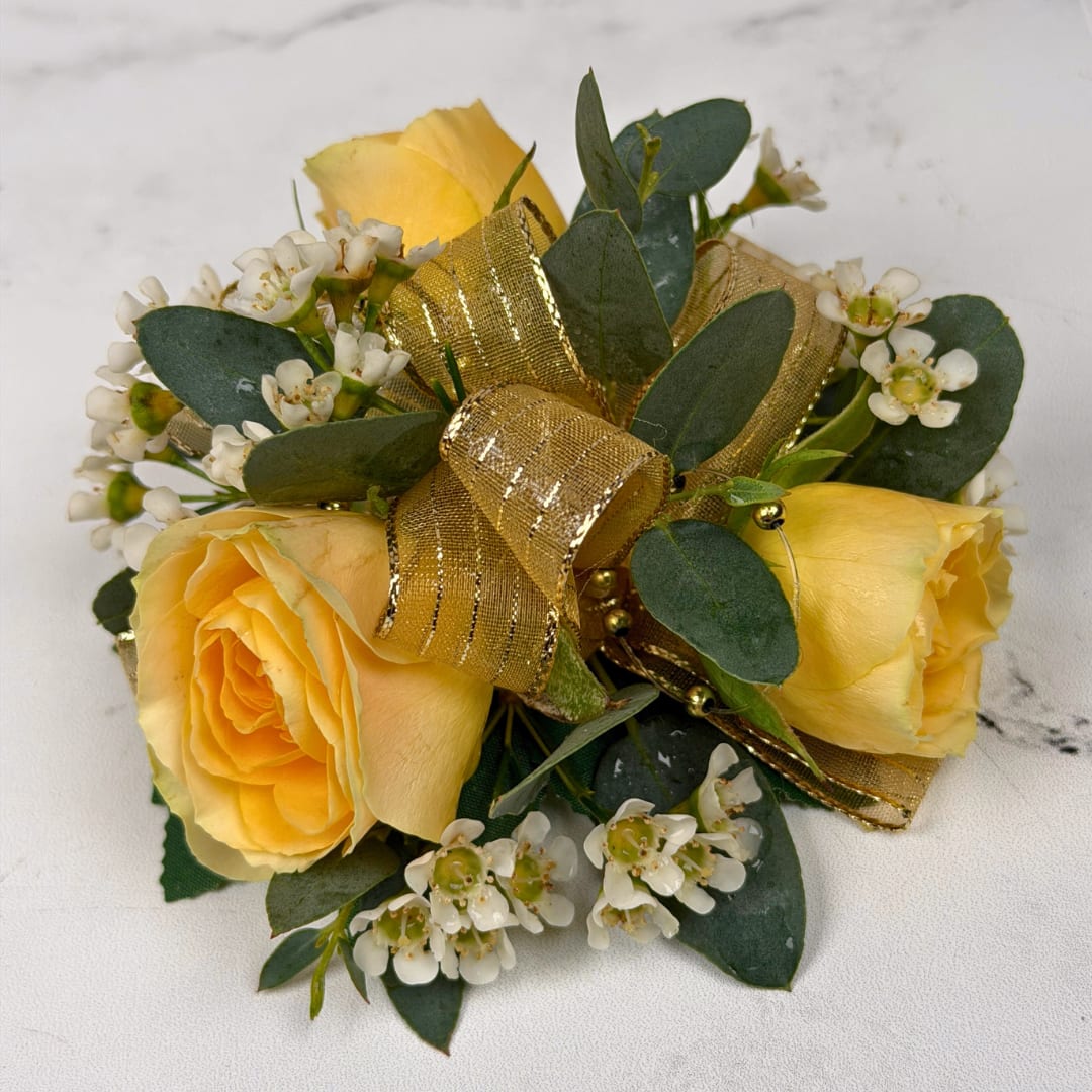 Topaz 3 Rose Corsage - Three pale yellow spray roses form the heart of this wrist corsage, a soft romantic accent perfect for proms or other dressy events. The yellow-and-white palette reads cheerful yet refined, so the person wearing it will feel celebrated and elegantly styled for their special moment.  Clusters of small white filler blossoms and rounded dark green foliage nestle around the roses for delicate texture and contrast. A sheer, shimmering gold ribbon is woven through design along with golden beaded accents to add a polished, festive shimmer. The compact, wrist-sized composition is hand-finished on a white, lace wristlet for a natural, comfortable fit, ideal for carrying through a long evening of dancing.