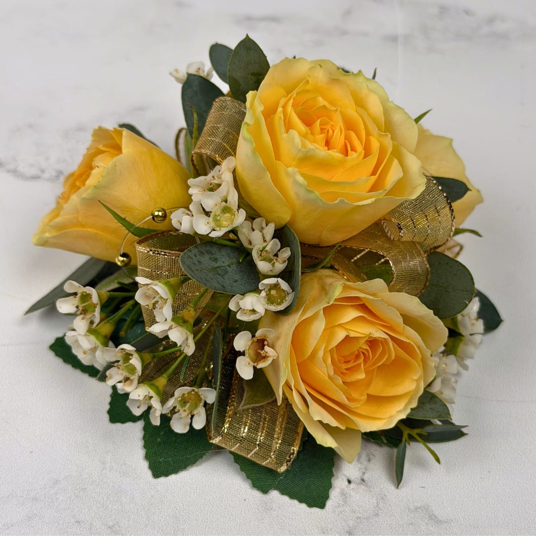 Topaz 4 Rose Corsage - Four pale yellow spray roses form the heart of this wrist corsage, a soft romantic accent perfect for proms or other dressy events. The yellow-and-white palette reads cheerful yet refined, so the person wearing it will feel celebrated and elegantly styled for their special moment.  Clusters of small white filler blossoms and rounded dark green foliage nestle around the roses for delicate texture and contrast. A sheer, shimmering gold ribbon is woven through design along with golden beaded accents to add a polished, festive shimmer. The compact, wrist-sized composition is hand-finished on a white, lace wristlet for a natural, comfortable fit, ideal for carrying through a long evening of dancing.