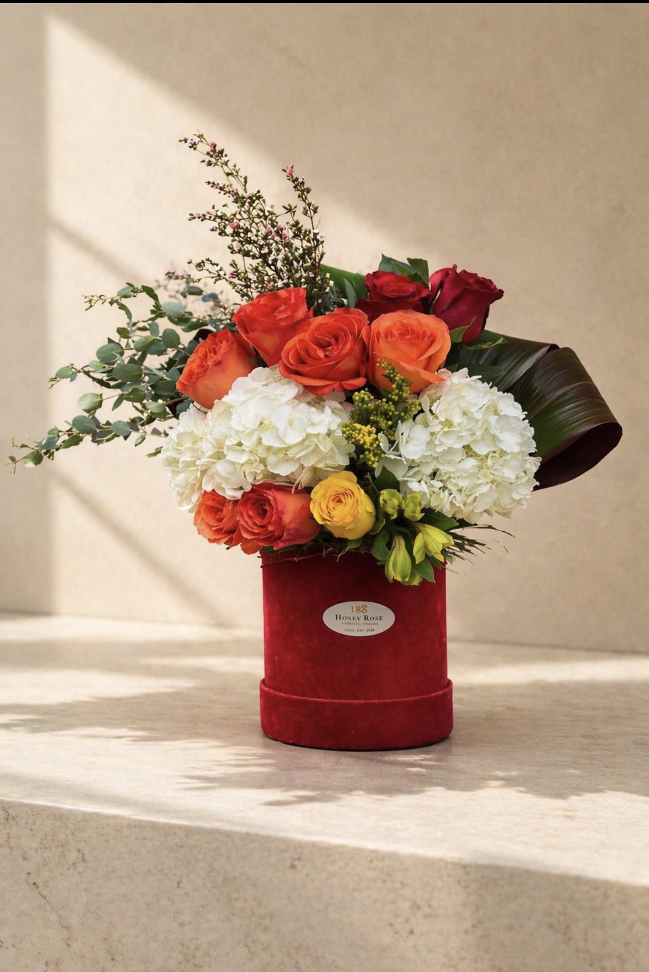 Sunset Elegance Floral Box - A refined and elegant floral arrangement featuring vibrant orange and red roses paired with soft white hydrangeas and fresh greenery, beautifully arranged in a luxurious velvet box.