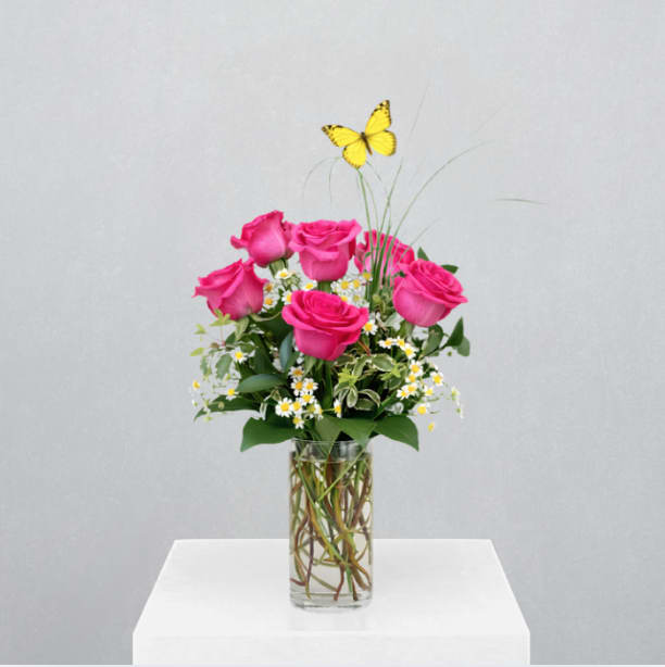 Butterfly Kisses - MOTHER'S DAY COLLECTION | LOCAL DELIVERY ONLY  A simple, yet charming design arranged in a 3x9 cylinder vase with natural curly willow and bear grass for an organic feel. Featuring 6-short stem roses, feverfew, mixed greenery, and a butterfly accent, this arrangement is a sweet gesture for Mom.