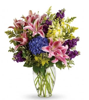 Pink lilies and purple flowers in a clear glass vase