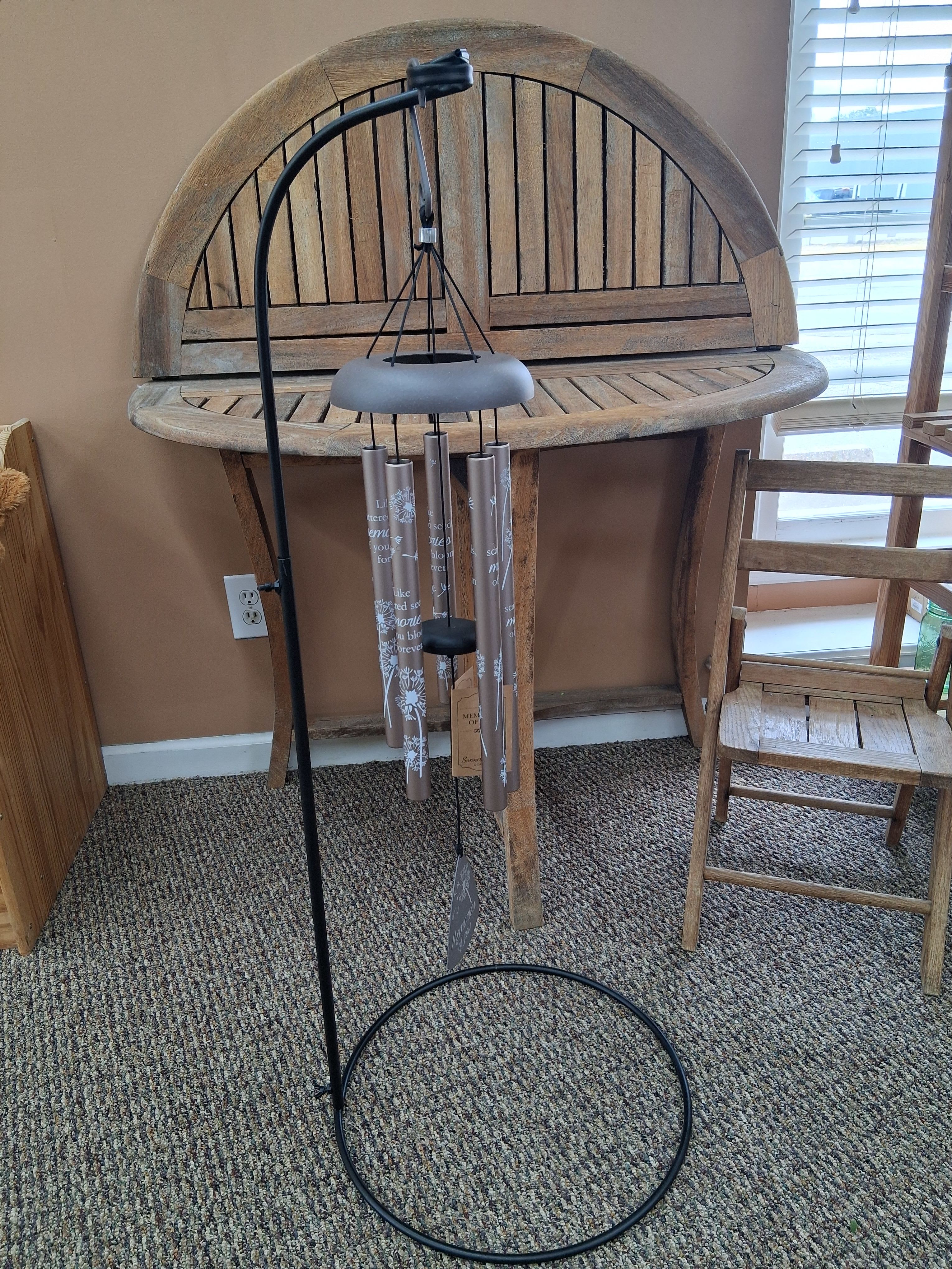Black metal wind chime hanging in front of a wooden table and chair