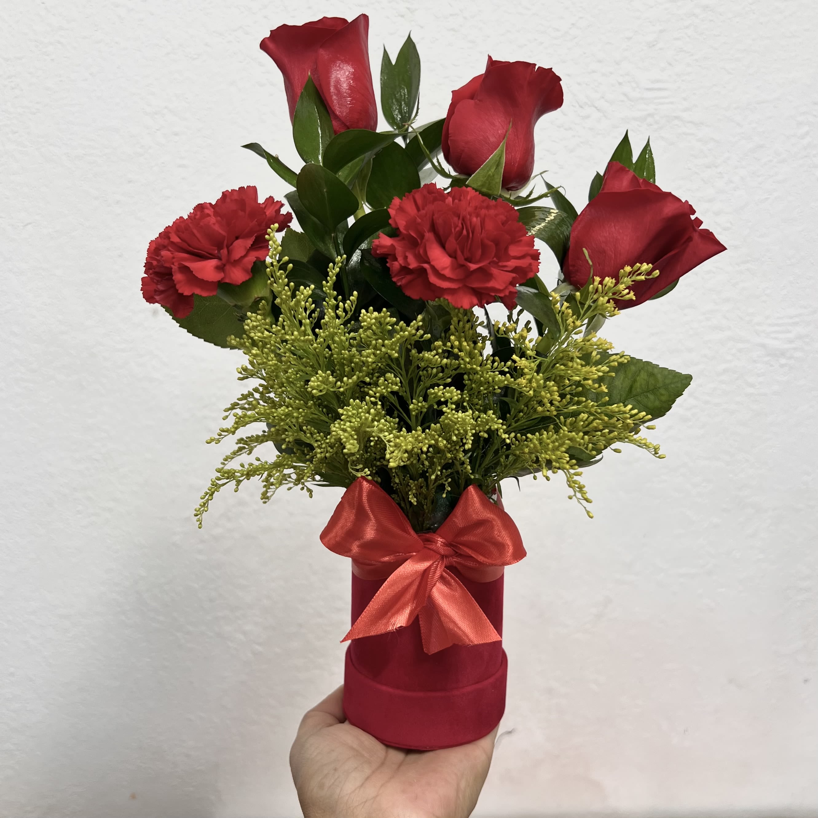 Crimson Charm Cilynder - Red Roses And Red Carnations - A vibrant mix of red roses and carnations, accented with fresh greenery, arranged in a stylish red box with a satin bow. A perfect gift to show love, admiration, and warmth.