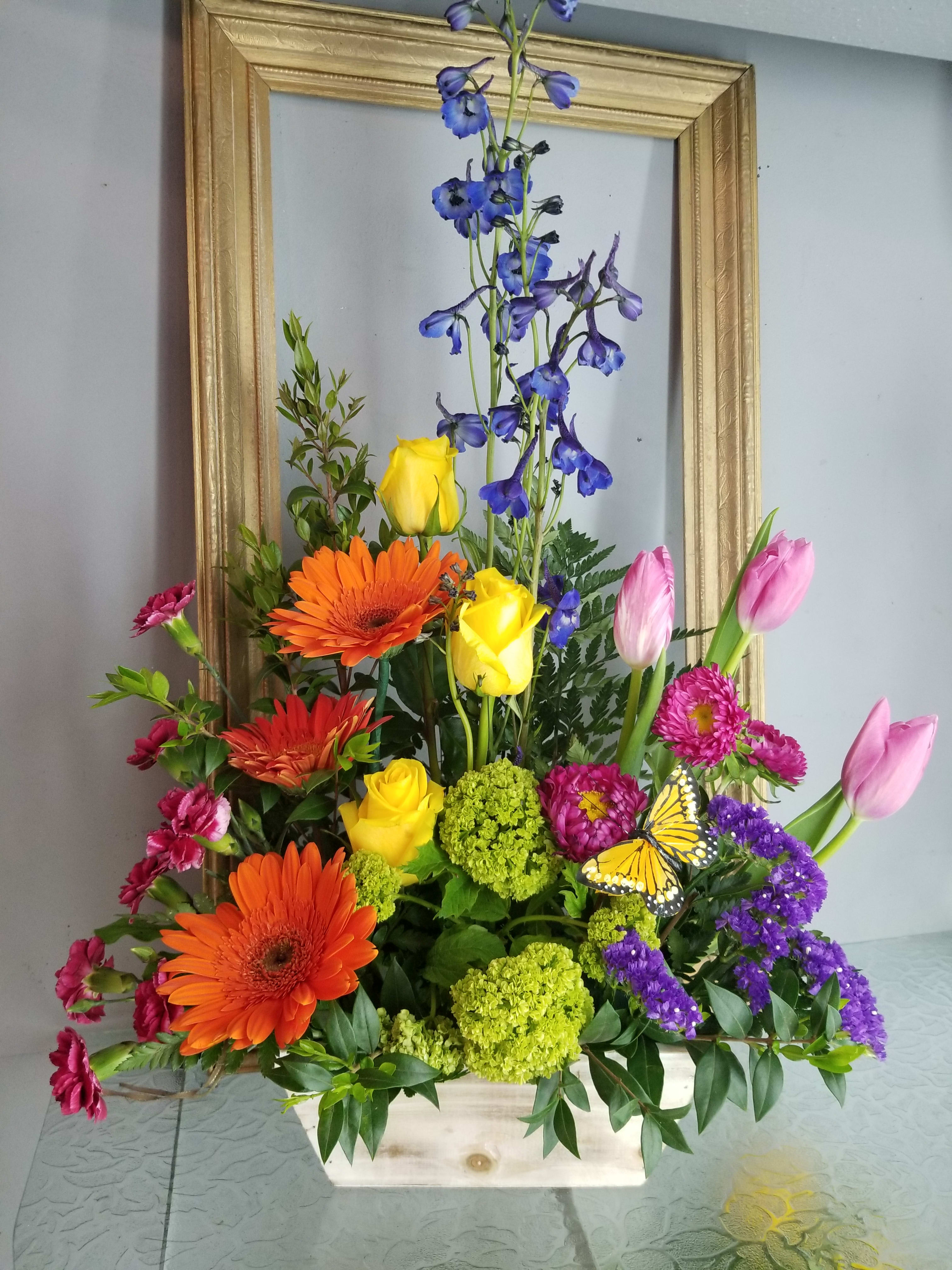 Colorful mixed flower arrangement in a wooden box with tall blue blooms