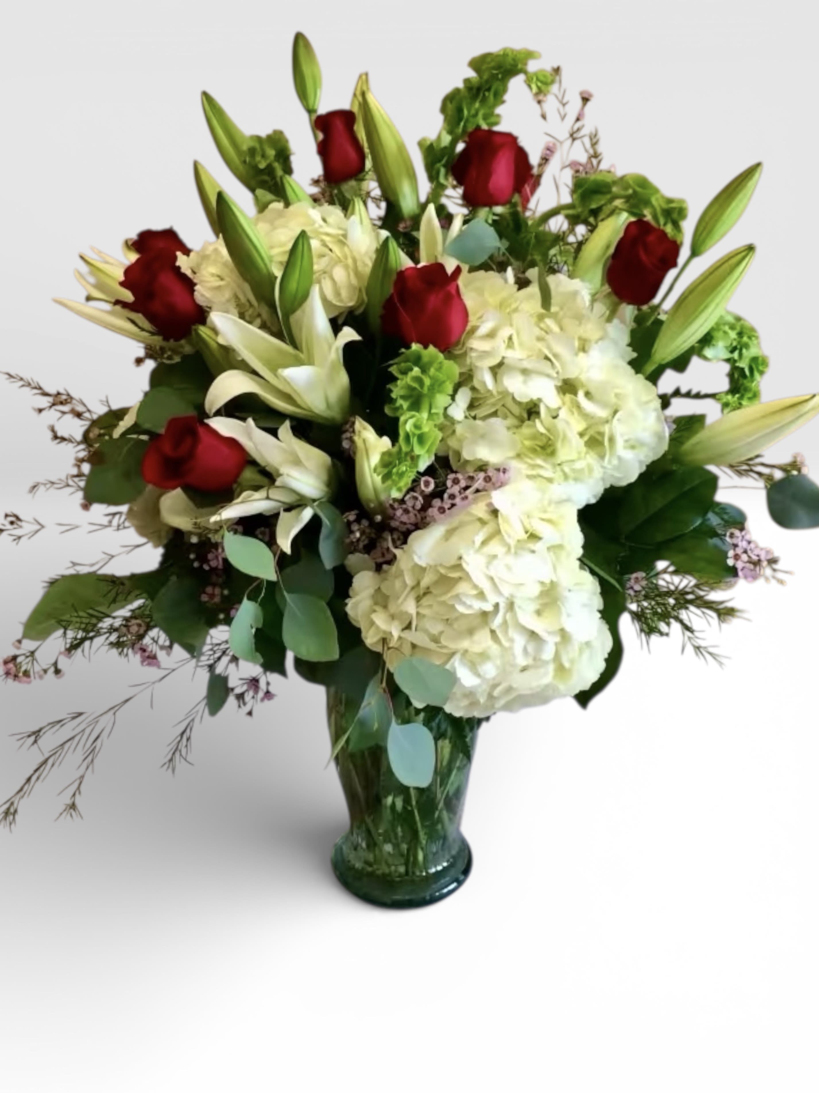 Red roses and white lilies with hydrangeas in a green glass vase