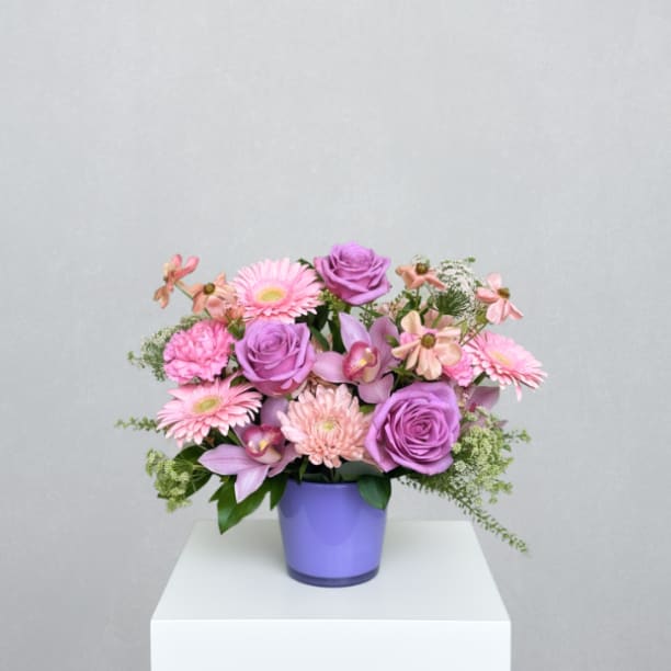 Pretty Like Mom - MOTHER'S DAY COLLECTION | LOCAL DELIVERY ONLY  A feminine, garden-inspired arrangement designed to celebrate Mom’s beauty, grace, and individuality. Designed in a colored Churchill vase, it features cremon mums, large gerbera daisies, short stem roses, cymbidium orchid blooms, ranunculus, Queen Anne’s lace, pennycress, and mixed greenery for a textured, layered, and expressive design. A heartfelt Mother’s Day statement full of personality and charm.