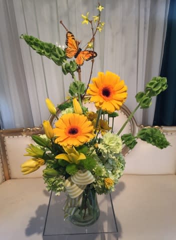 Yellow floral arrangement with orange gerbera daisies in a glass vase