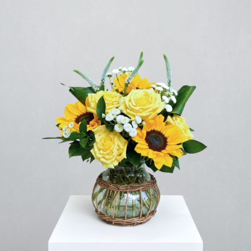 Sunny Memories - MOTHER'S DAY COLLECTION | LOCAL DELIVERY ONLY  A bright and joyful Mother’s Day arrangement designed to celebrate warmth, nostalgia, and happy moments shared with Mom. Designed in a keepsake wicker vase, it features sunflowers, yellow short stem roses, veronica, feverfew, and mixed greenery for a radiant, sun-filled feel that feels both uplifting and sentimental.
