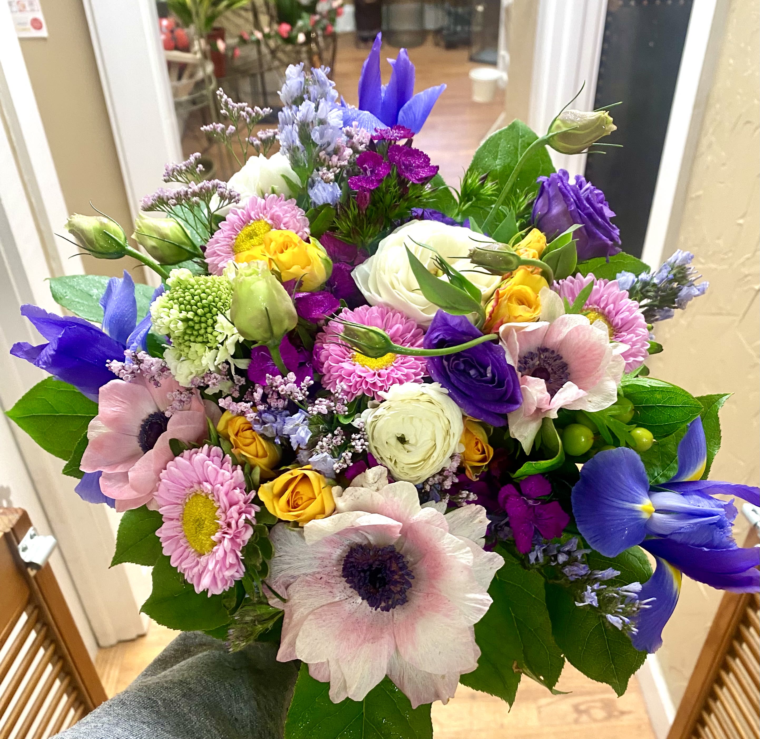 Hand-tied bouquet of purple iris, pink anemones, yellow roses, and assorted bright blooms.