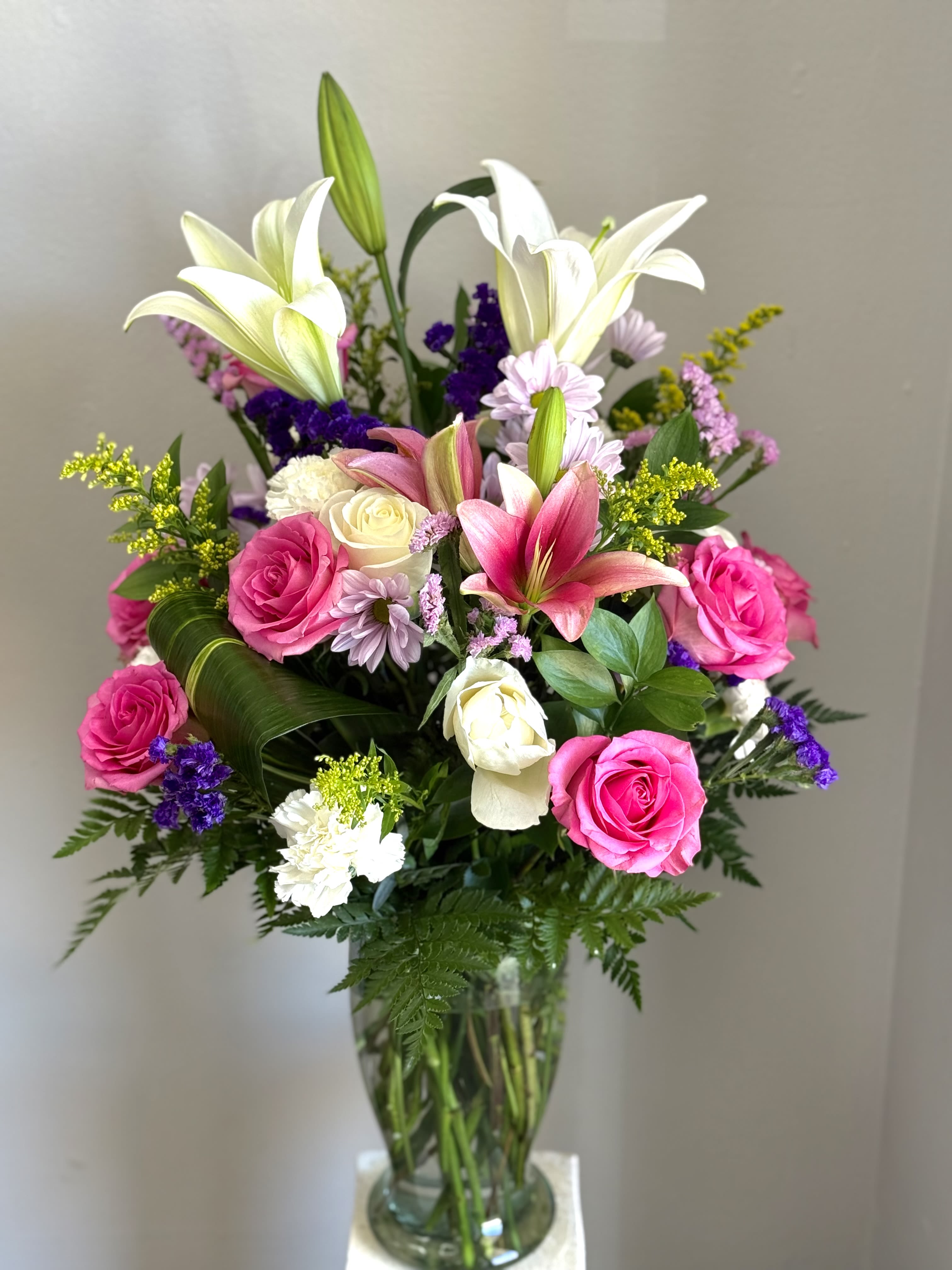 . Lily &amp; Rose Delight - Tall white lilies arching above a rounded cluster of bright pink roses give this flower arrangement a fresh, cheerful, slightly romantic presence-perfect as a birthday bouquet, anniversary flowers, or a thoughtful thank-you gift. The upright, layered composition makes the recipient feel noticed and celebrated the moment they see it, whether sent to a friend, partner, or colleague.  A full mix of white lilies, vivid pink roses, pale daisies, soft carnations and small purple filler blooms are arranged in a clear glass vase, creating pleasing height and a lush, textural contrast between the lilies' graceful trumpets and the compact rose heads. The pink, white, purple and touches of yellow play together for a springlike look that brightens any room; sizing is generous with the lilies rising above the rounded mass of blooms for a striking silhouette.  This versatile arrangement is an easy way to say "thinking of you" or "congratulations" without overdoing it-she'll feel genuinely celebrated. Vase-ready and delivered arranged, simply trim stems as needed and refresh water every 2-3 days to keep the flowers looking their best.