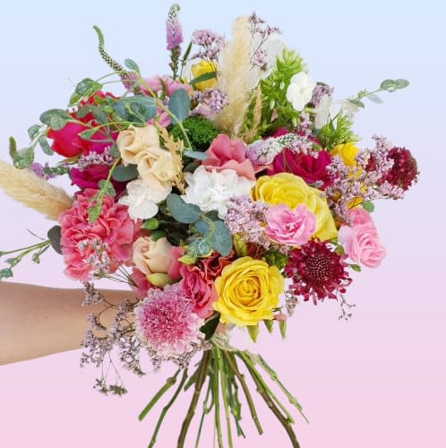 Handheld bouquet of pink, yellow, white, and red flowers