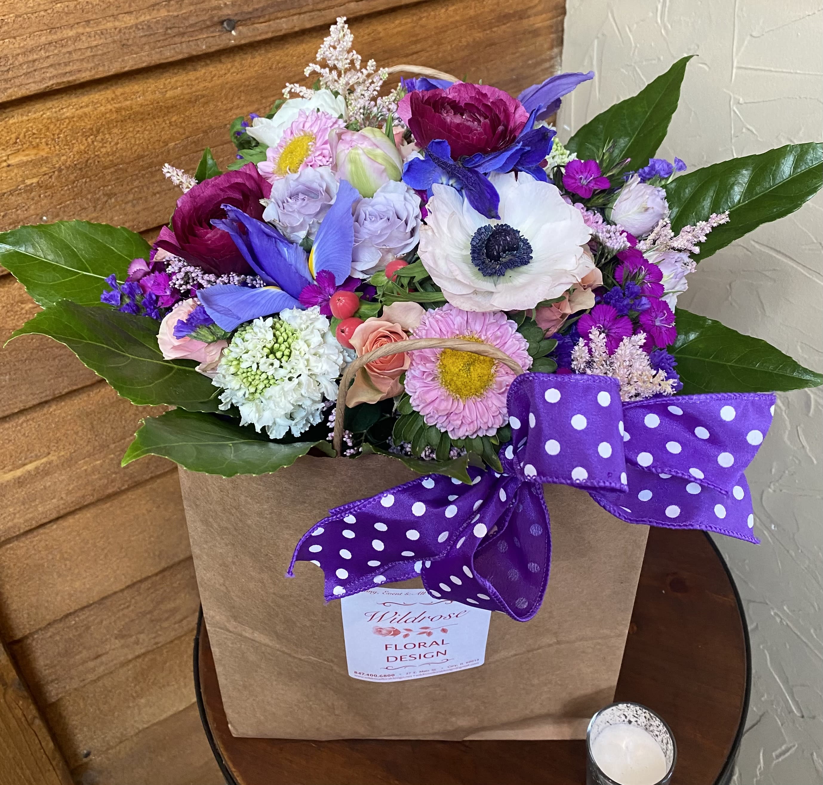 Colorful mixed flower arrangement in a kraft bag with a purple polka dot bow.