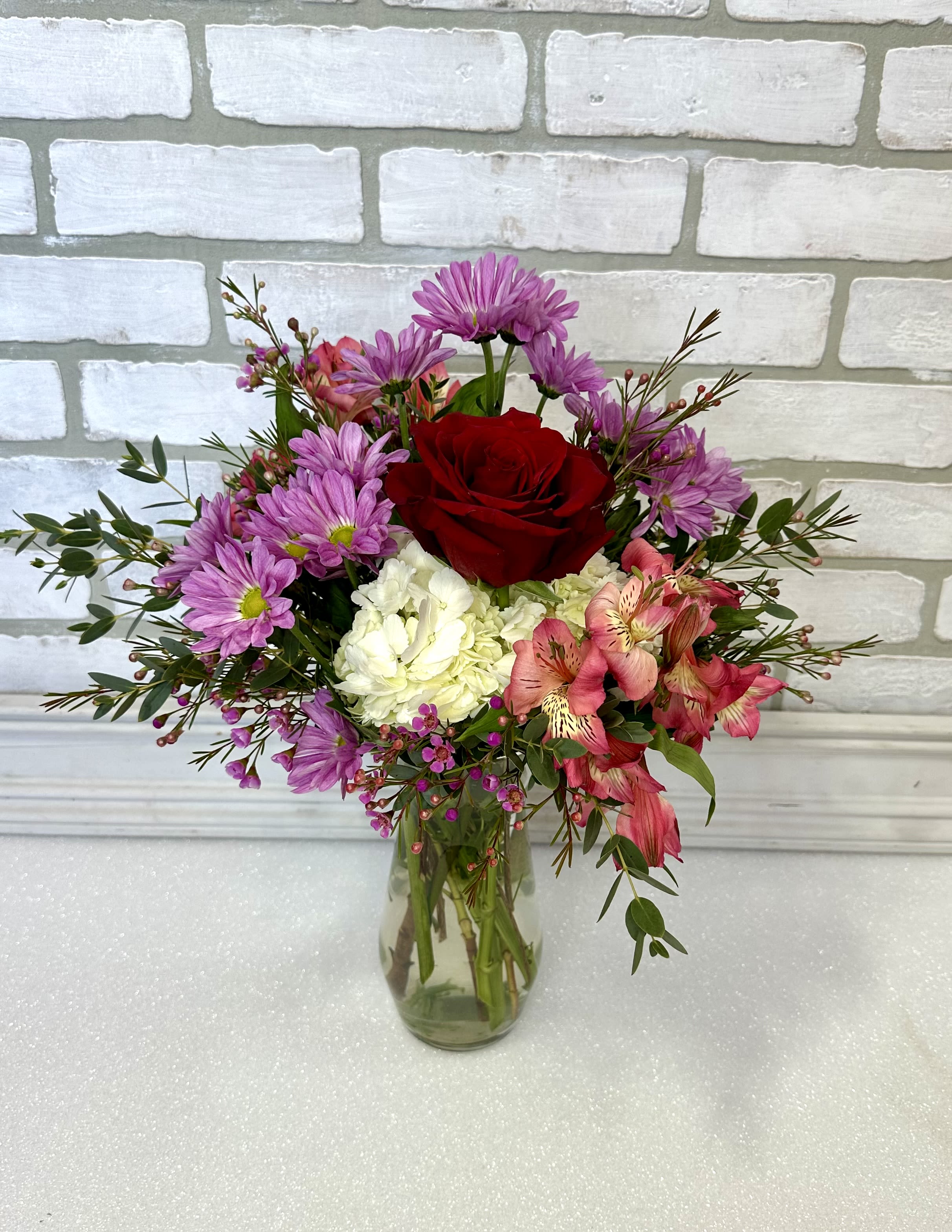 Mixed bouquet of red, pink, purple, and white flowers in a clear glass vase