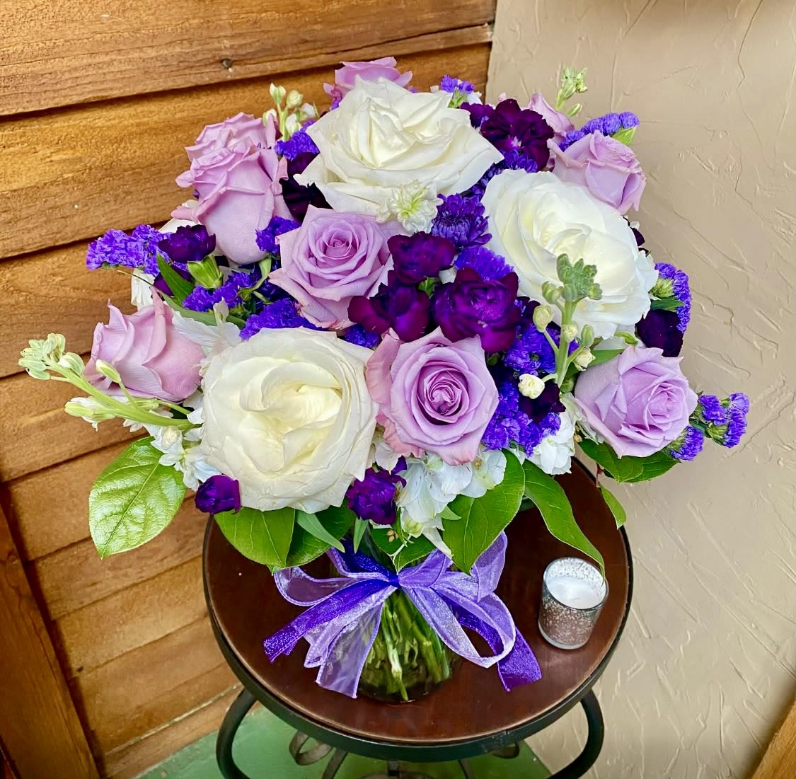 Bouquet of white, lavender, and purple roses in a glass vase with a purple ribbon