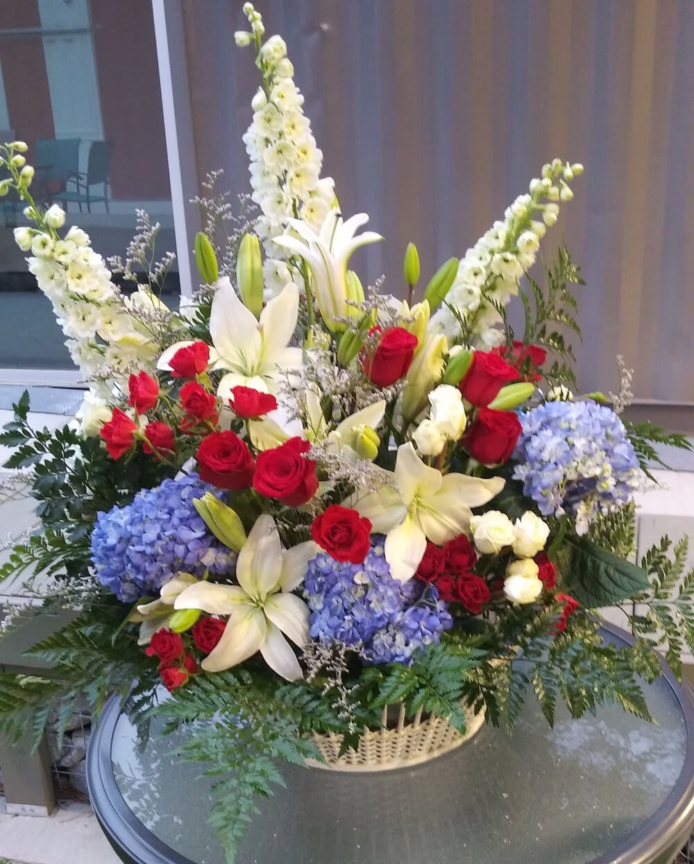 Large floral arrangement with red roses, white lilies, and blue hydrangeas in a basket