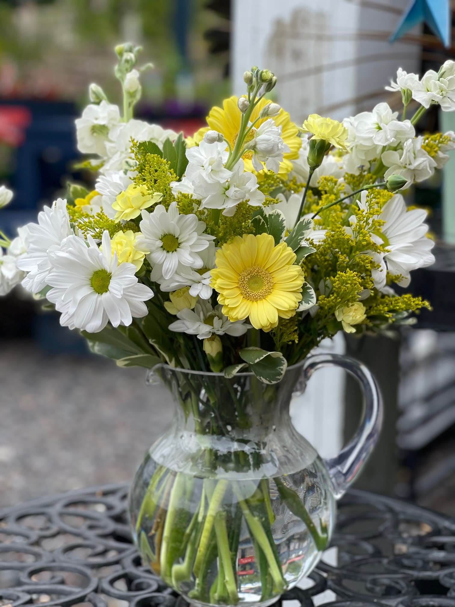 Yellow and white daisies in a clear glass pitcher vase