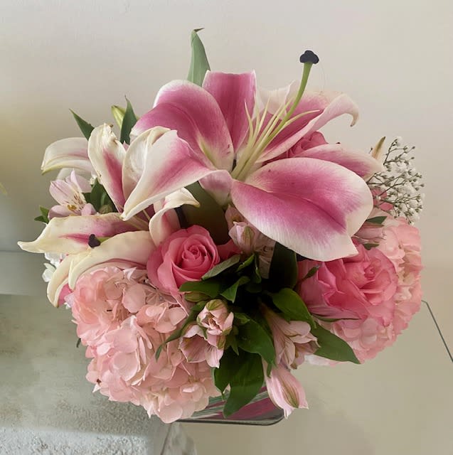 Pink and white lilies, roses, and hydrangeas arranged in a short glass cube vase