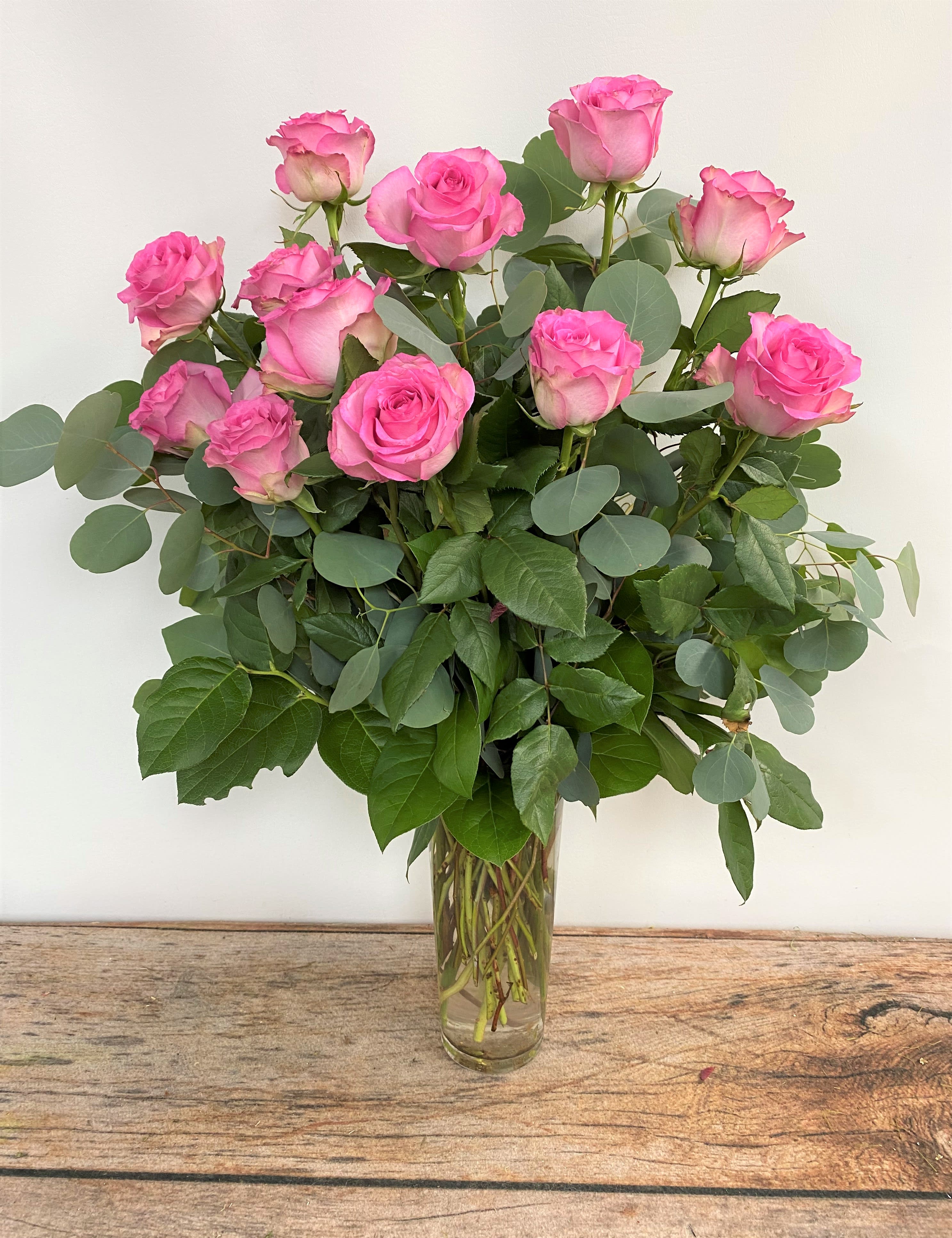 Pink roses arranged in a clear glass vase with eucalyptus foliage