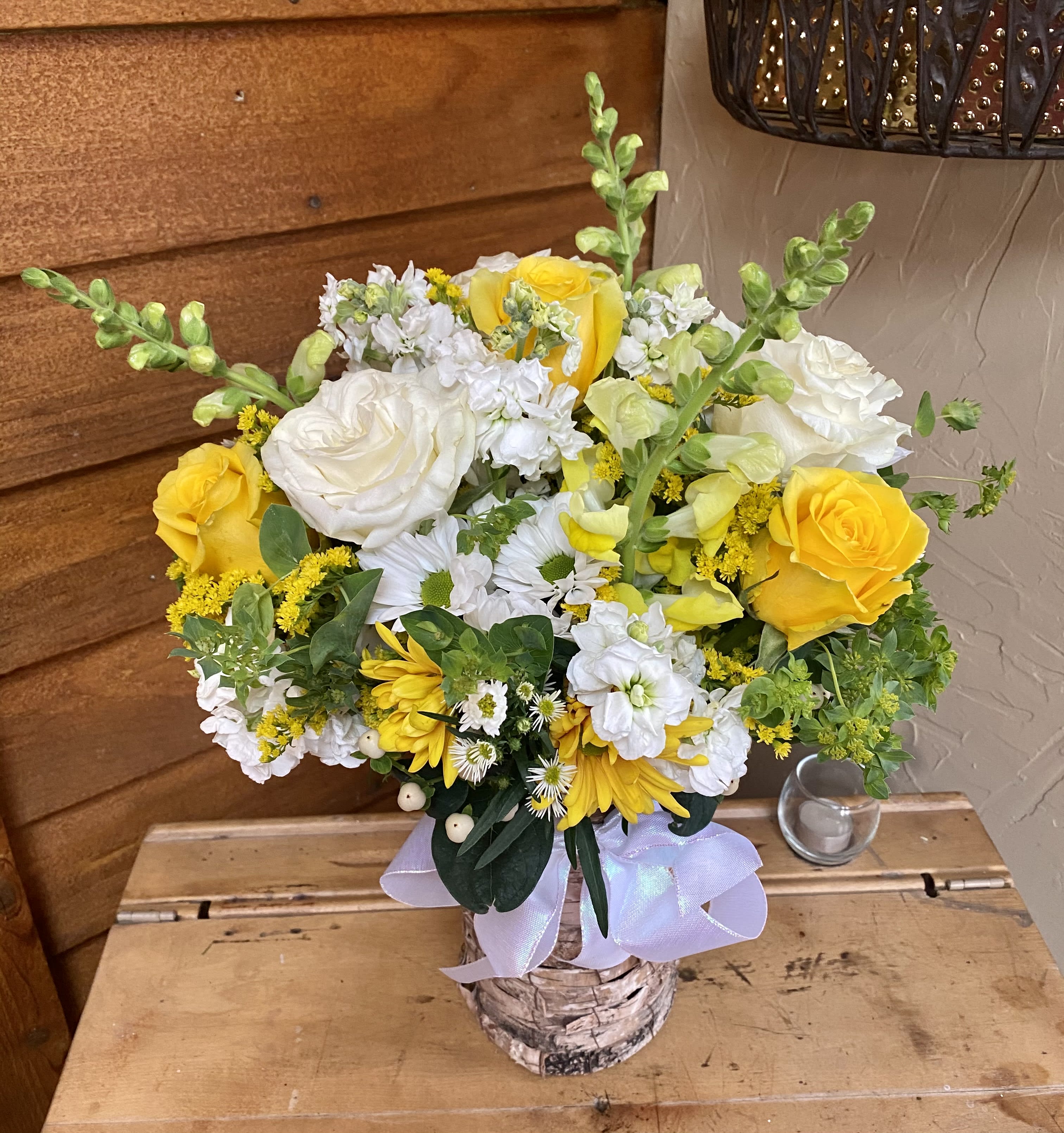 Yellow and white mixed flower arrangement in a birch-style container with a lavender ribbon