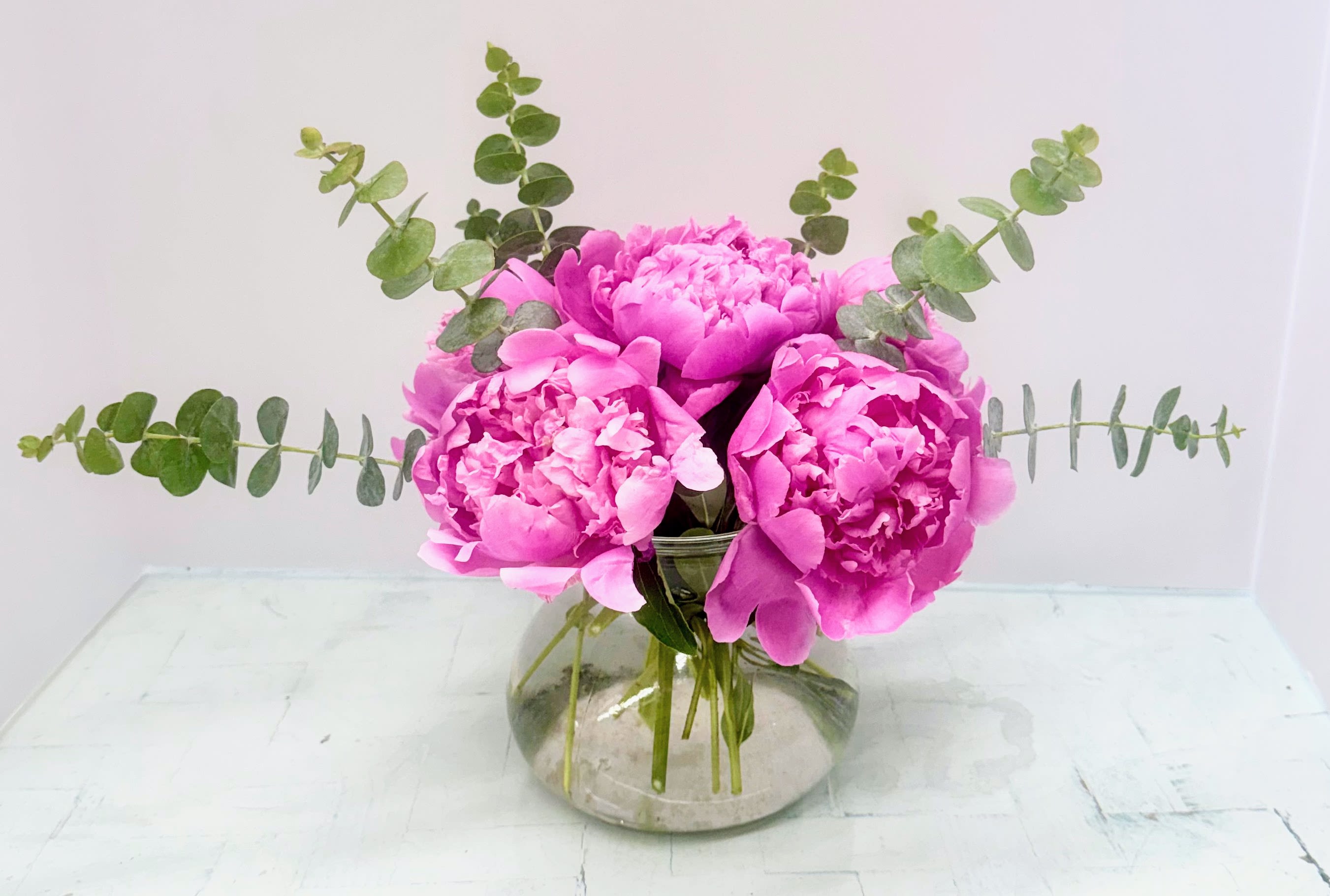 Pink peonies in a clear glass vase with eucalyptus stems