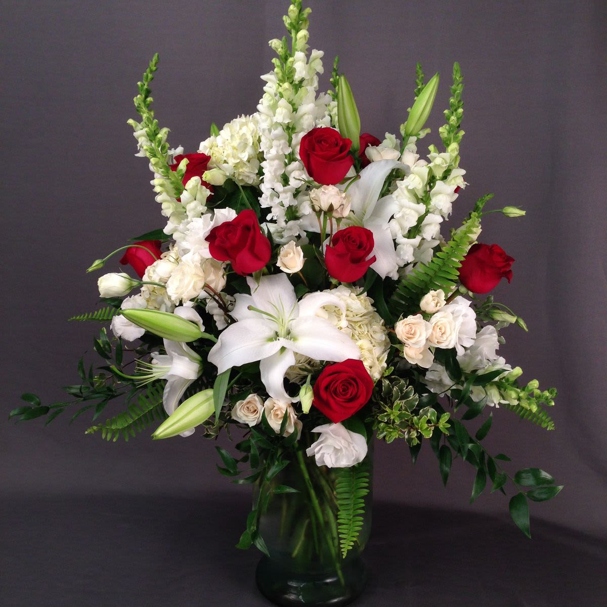 Saying Farewell Arrangement - This arrangement features a bold, traditional pairing of velvety red roses and pristine white lilies, offering a look of timeless elegance and respect.
