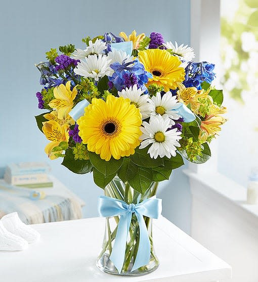 Bouquet of yellow gerbera daisies, white daisies, and blue flowers in a glass vase