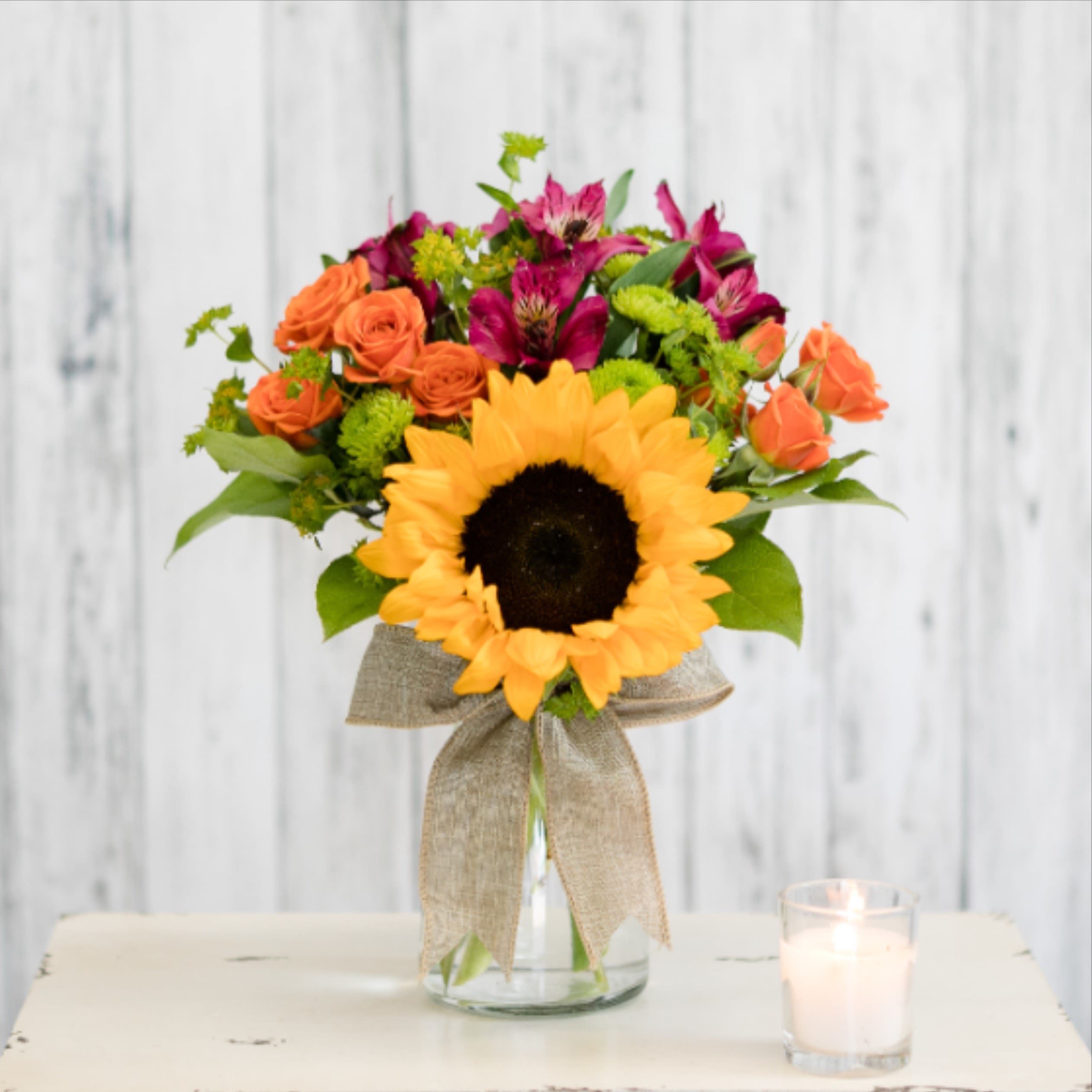 Brilliant - Vibrant and bold~ a vase filled with orange, purple and green blooms with a sunflower front and center is sure to bring a smile!  Approximate Dimensions: 12" H X 9" W