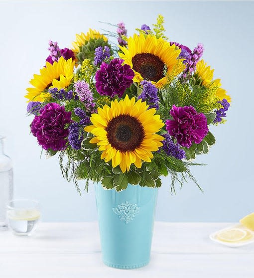 Sunflowers and purple flowers arranged in a blue vase