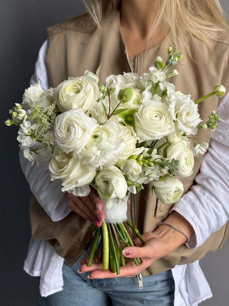 Ethereal Ivory Grace  - This white bridal bouquet is a refined and luxurious choice for weddings in Orlando and surrounding areas. Designed with premium ranunculus, garden roses, delicate lisianthus, and fragrant stock, this composition features a soft, airy European style with natural movement and elegant texture. Lisianthus adds a romantic, silky softness, while stock brings subtle fragrance and volume, creating a bouquet that feels rich yet effortlessly light. Each stem is carefully selected by an experienced Orlando wedding florist to ensure exceptional quality, freshness, and a harmonious ivory palette. Perfect for brides seeking a luxury bridal bouquet, this design complements both classic and modern wedding aesthetics and photographs beautifully in any setting. Ideal for weddings in Orlando, Altamonte Springs, Winter Park, and surrounding venues.