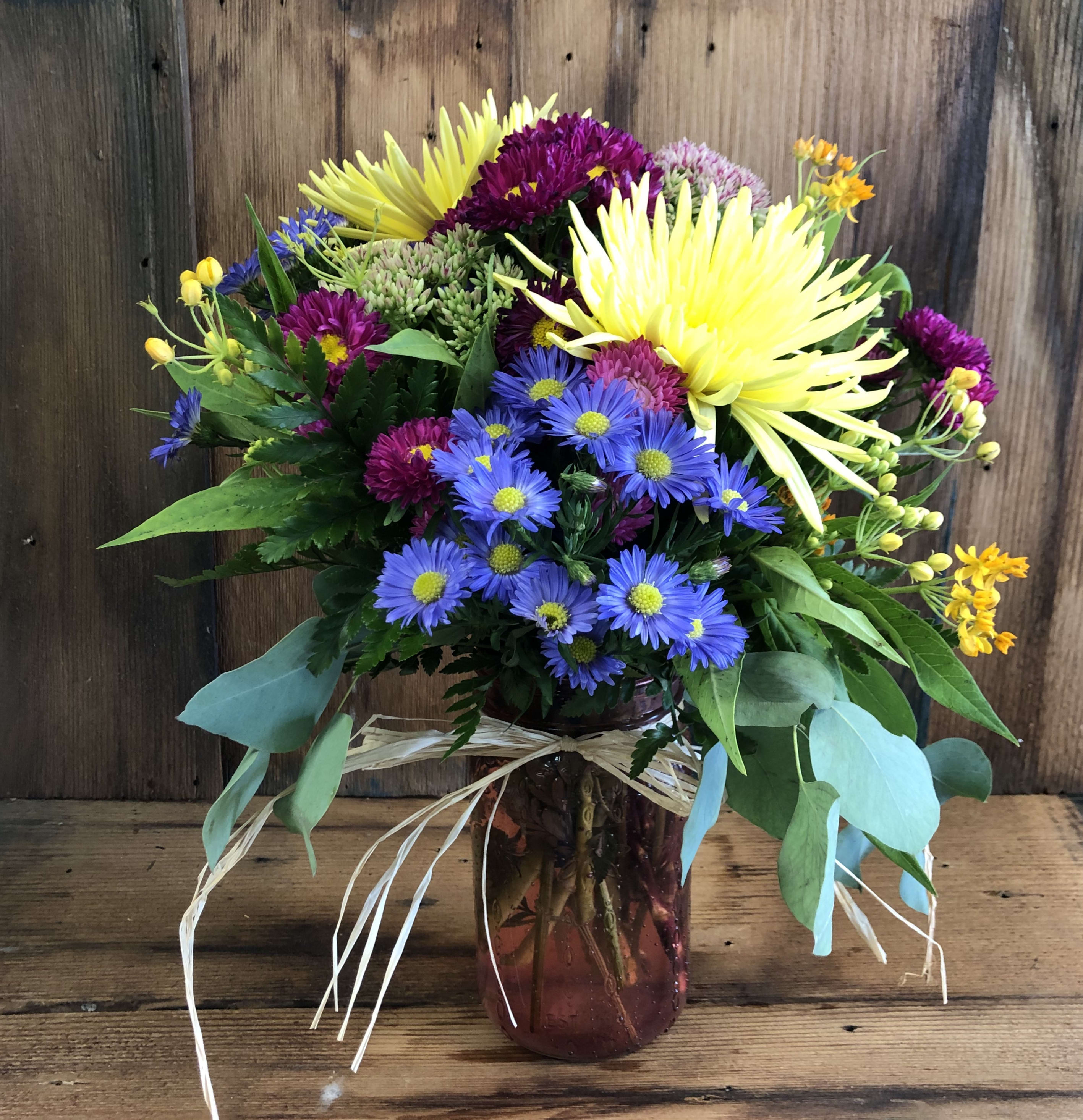 Designers Choice Bloom Jar - This sweet little mason jar is the perfect gift for any occasion! Let us pick the freshest seasonal flowers and coloring to suit the occasion. Arrangement shown represents the general look and feel- actual coloring and flowers may vary. Standard shown. Deluxe adds more flowers to enhance the arrangement. Premium includes the deluxe value arrangement and we'll add a box of 8 oz. mixed chocolates.