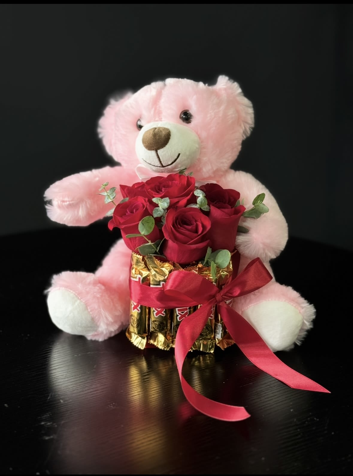Sweet Love Gift Set - Sweet Love Gift Set is a beautifully curated romantic arrangement that combines fresh flowers, premium chocolates, and a soft plush teddy bear into one elegant and thoughtful gift. The composition features a cuddly teddy bear paired with a handcrafted arrangement of fresh red roses accented with eucalyptus greenery. The roses are arranged in a stylish chocolate box, creating a rich and visually striking presentation. The deep red tones symbolize love and passion, while the greenery adds a soft, natural balance. Finished with a satin ribbon, this design is ready to gift  Each set is handcrafted and may vary slightly to ensure freshness and high quality.