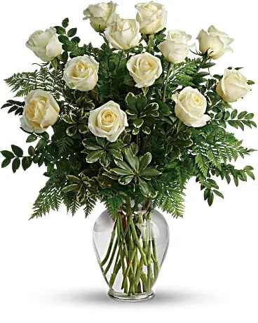 White roses arranged in a clear glass vase with lush greenery