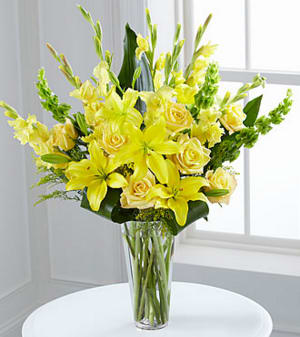 Yellow lilies and roses arranged in a clear glass vase