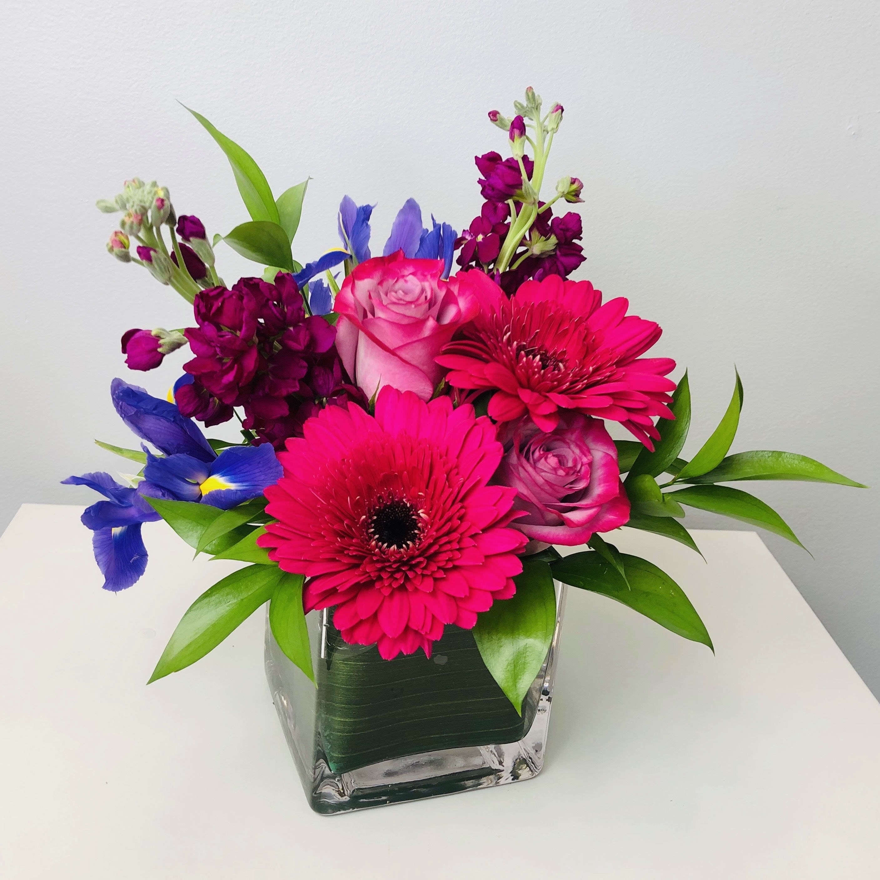 Color Burst - Bursting with bright and bold shades of purple, pink, blue and green, this arrangement is sure to brighten up someone’s day!  Approximately 10" Tall  Container Country of Origin: Mexico Flower Country of Origin: Canada, Ecuador, Columbia