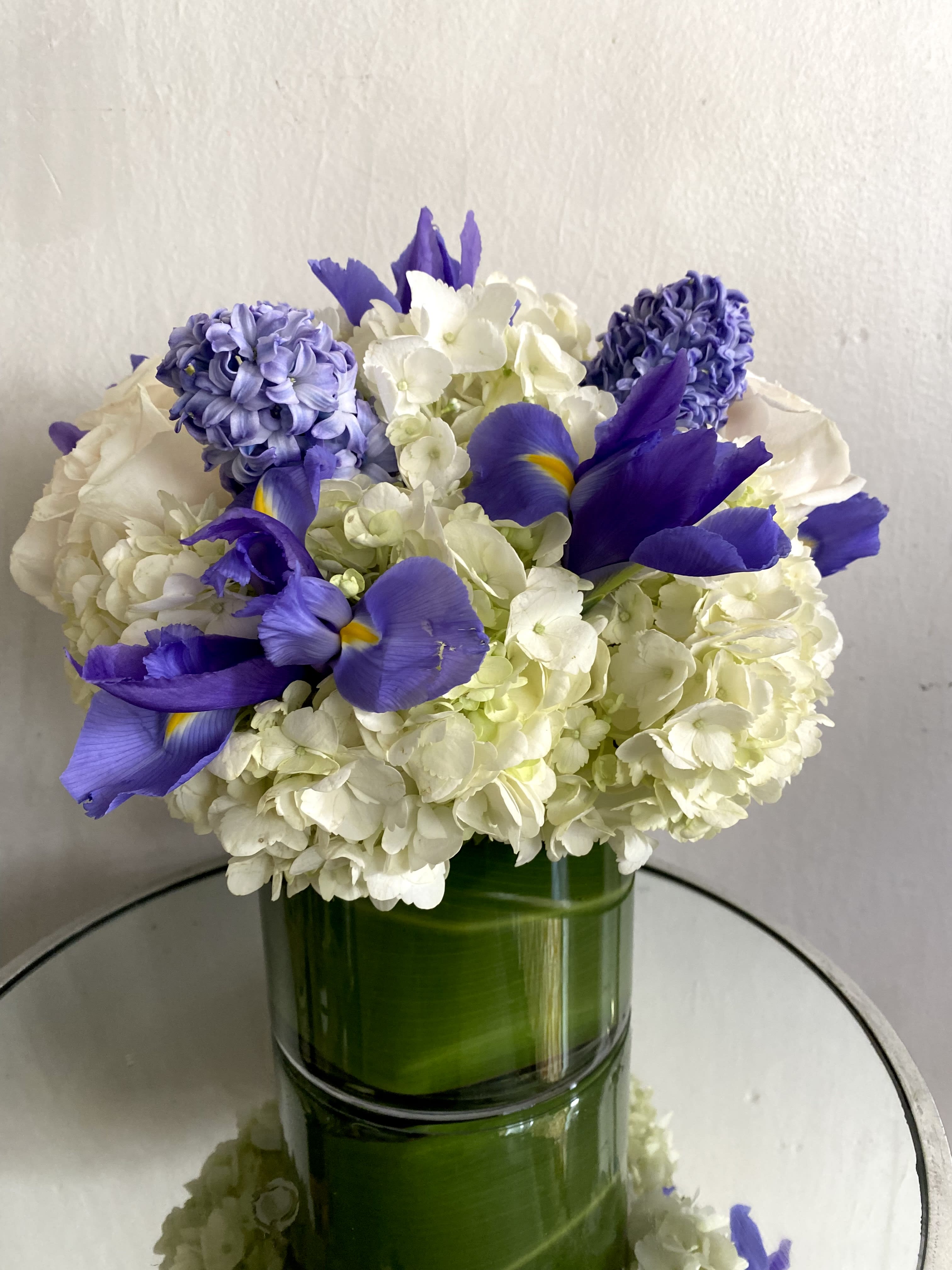 White hydrangeas and purple irises arranged in a green glass vase