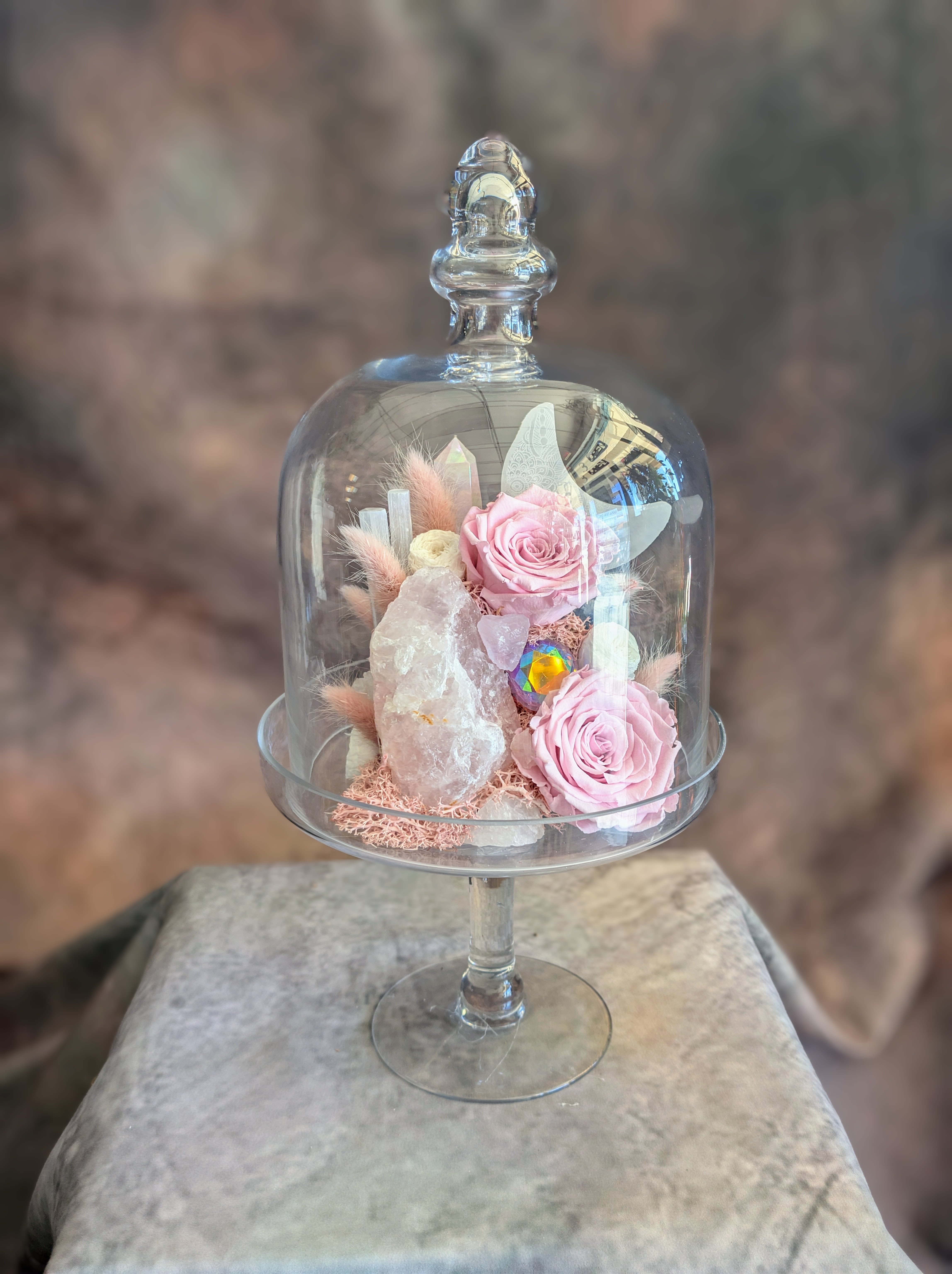 Octavia- A Preseved Flower And Crystal Arrangement - A study in soft opulence, Octavia is a refined composition of preserved blush roses, luminous rose quartz, selenite, and delicate textural botanicals, artfully arranged beneath a glass cloche. Each element is thoughtfully placed to create a sense of balance, light, and quiet romance—where natural beauty meets elevated design. The crystal accents add a subtle glow, catching light from every angle and giving this piece an almost ethereal presence.  Handcrafted in Las Vegas by Windmill Floral Expressions, Octavia is a lasting floral keepsake designed for meaningful gifting or sophisticated décor. This custom piece is one-of-a-kind, created with premium preserved botanicals and curated elements for a truly bespoke feel.  Perfect for birthdays, anniversaries, or simply indulging in something beautiful, Octavia is available for same-day delivery in Las Vegas and Henderson.