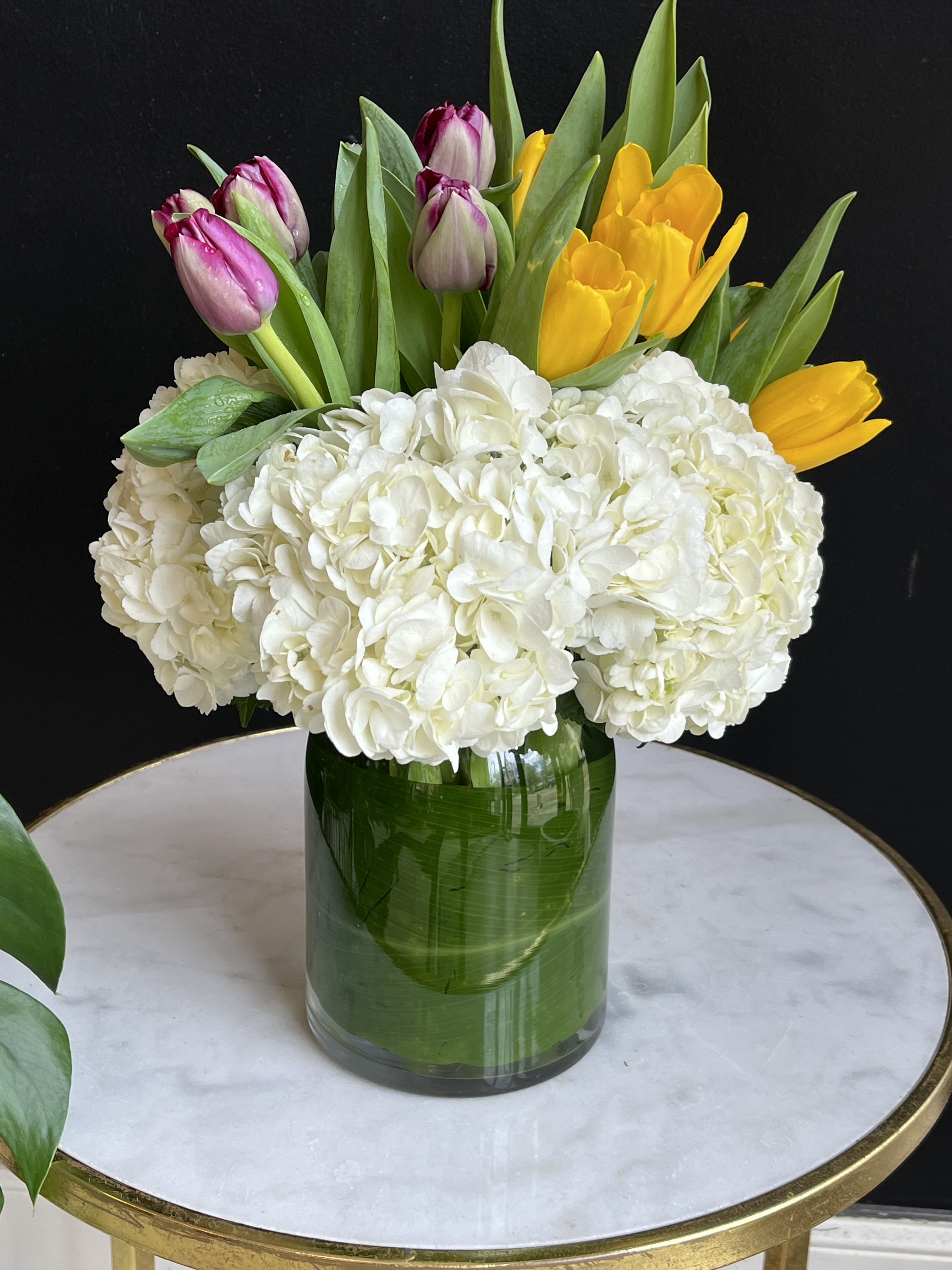 White hydrangeas with pink and yellow tulips in a glass vase
