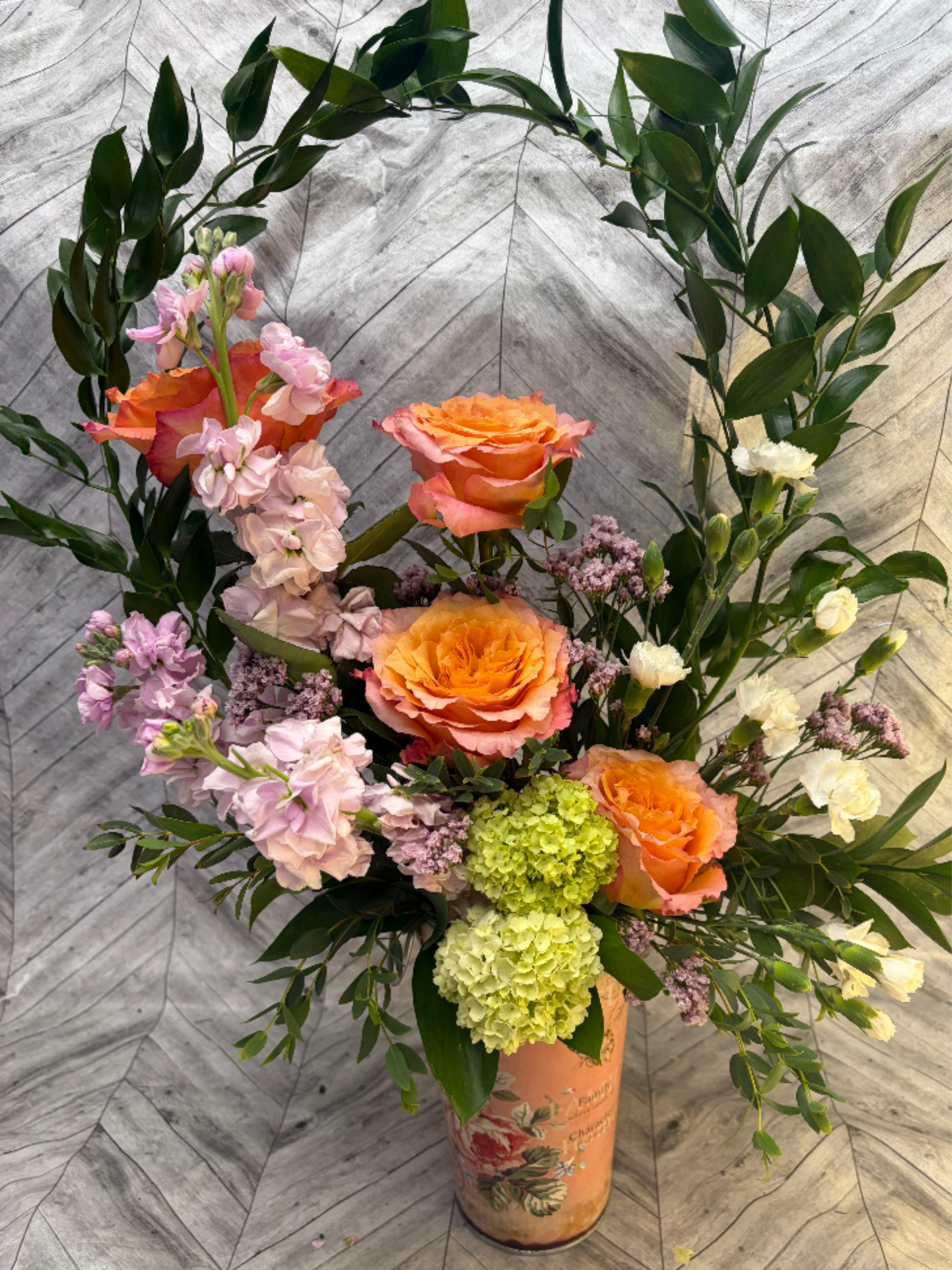 Belle Fleur - “Belle Fleur” — French for “Beautiful Flower” — is a stunning, garden-inspired arrangement that captures effortless elegance and vibrant charm.This lush design features: rich peach/coral roses as the romantic focal flowers, soft pink and lavender stock for graceful height and movement, and chartreuse/green hydrangea for a fresh, modern pop of color.  Presented in a charming decorative vase with a vintage floral motif, “Belle Fleur” has a soft, romantic color palette of warm peaches, pinks, and creamy whites that feels both timeless and uplifting. Perfect for Mother’s Day, birthdays, anniversaries, or any occasion where you want to send something truly special and beautiful.  