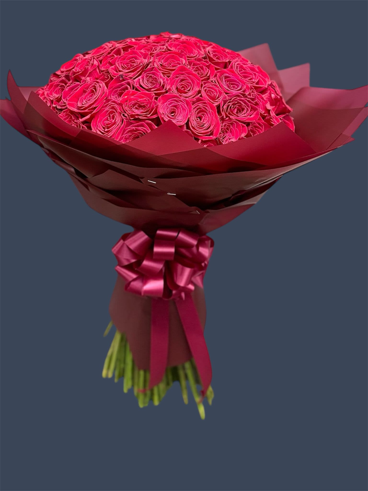 Bouquet of bright pink roses wrapped in burgundy paper with a ribbon