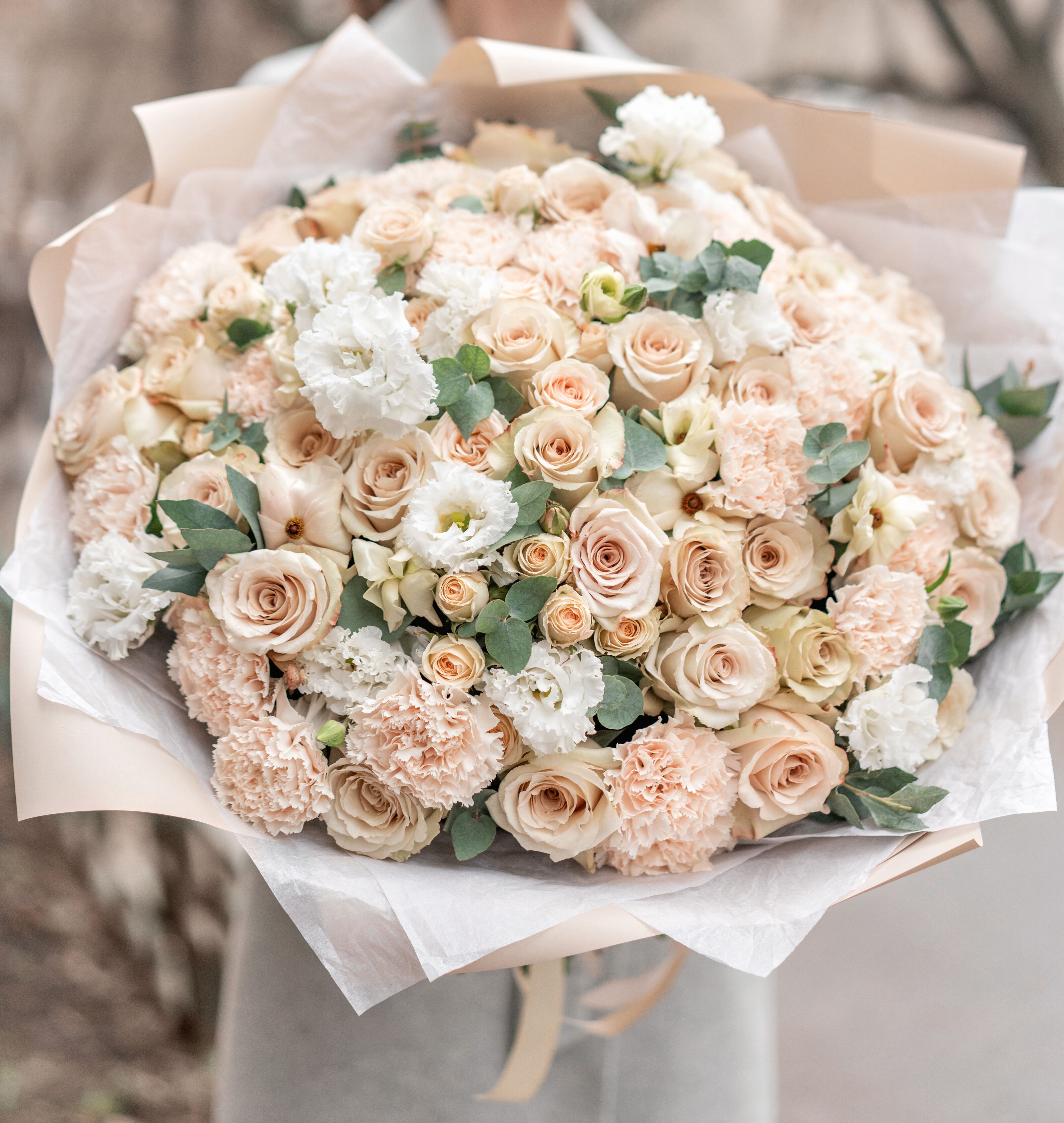Large bouquet of blush roses, carnations, and white blooms wrapped in paper