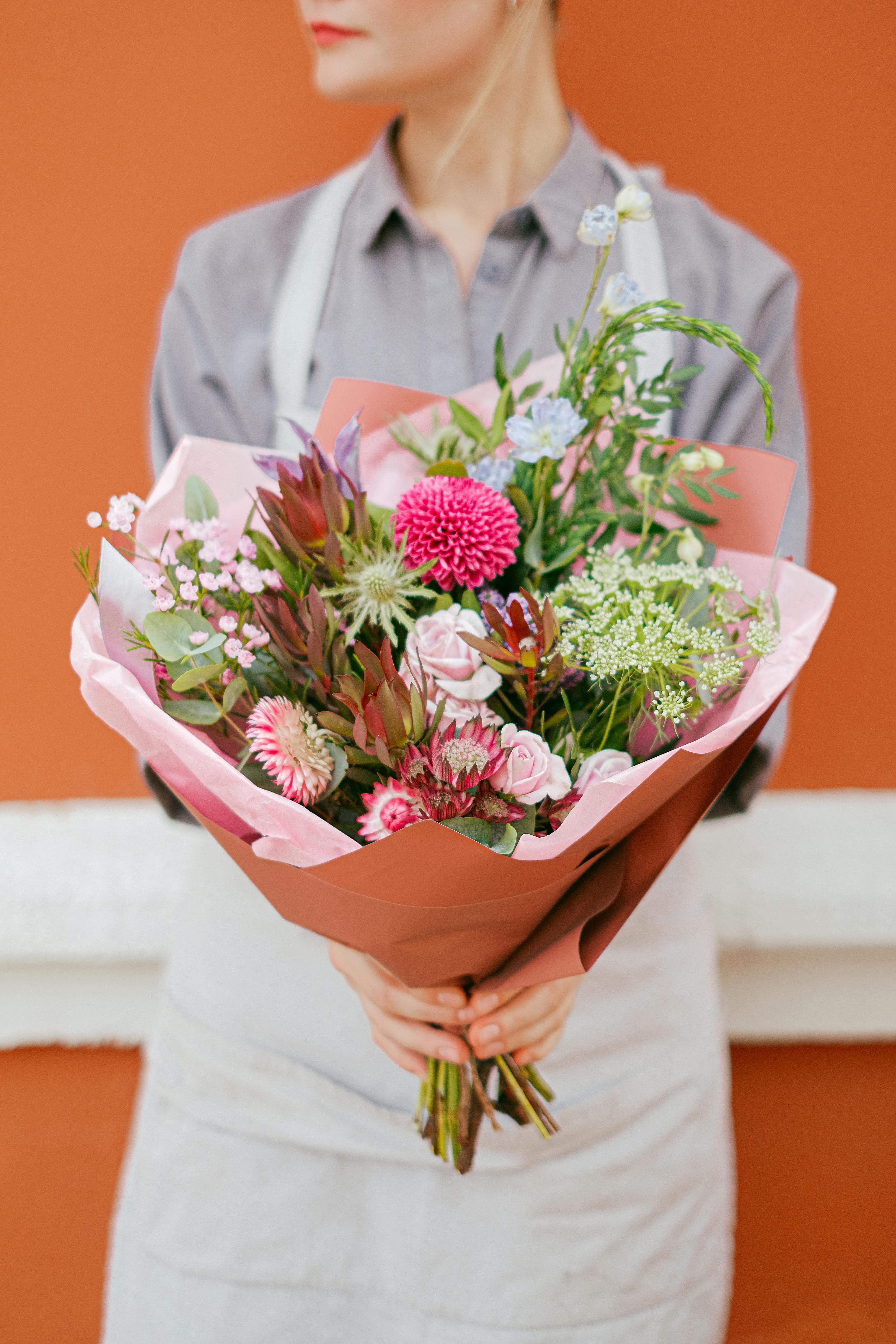 Handheld bouquet of pink and white flowers wrapped in peach paper